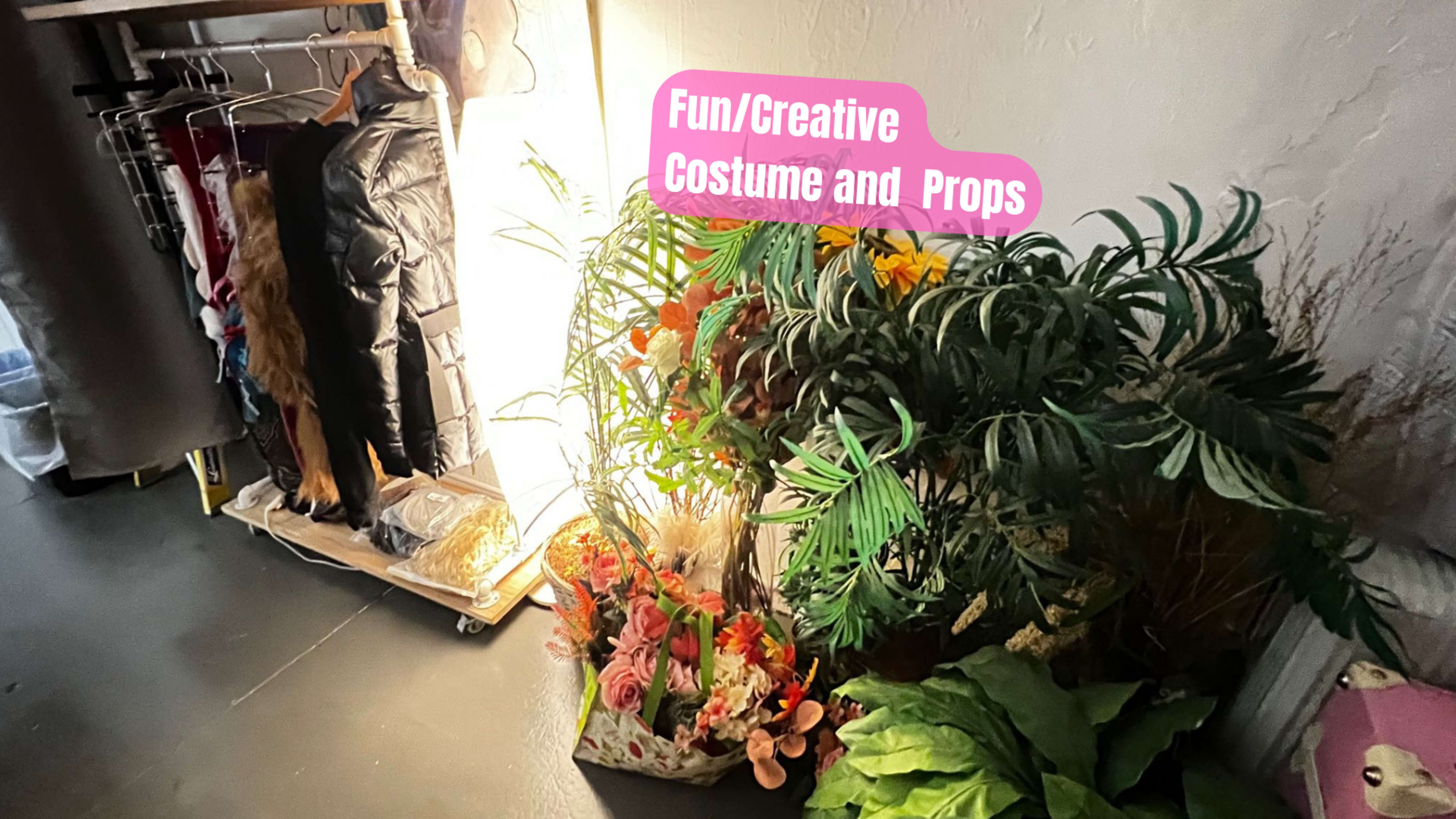 A corner of a room with a variety of costumes and props, including a potted plant and floral arrangements.