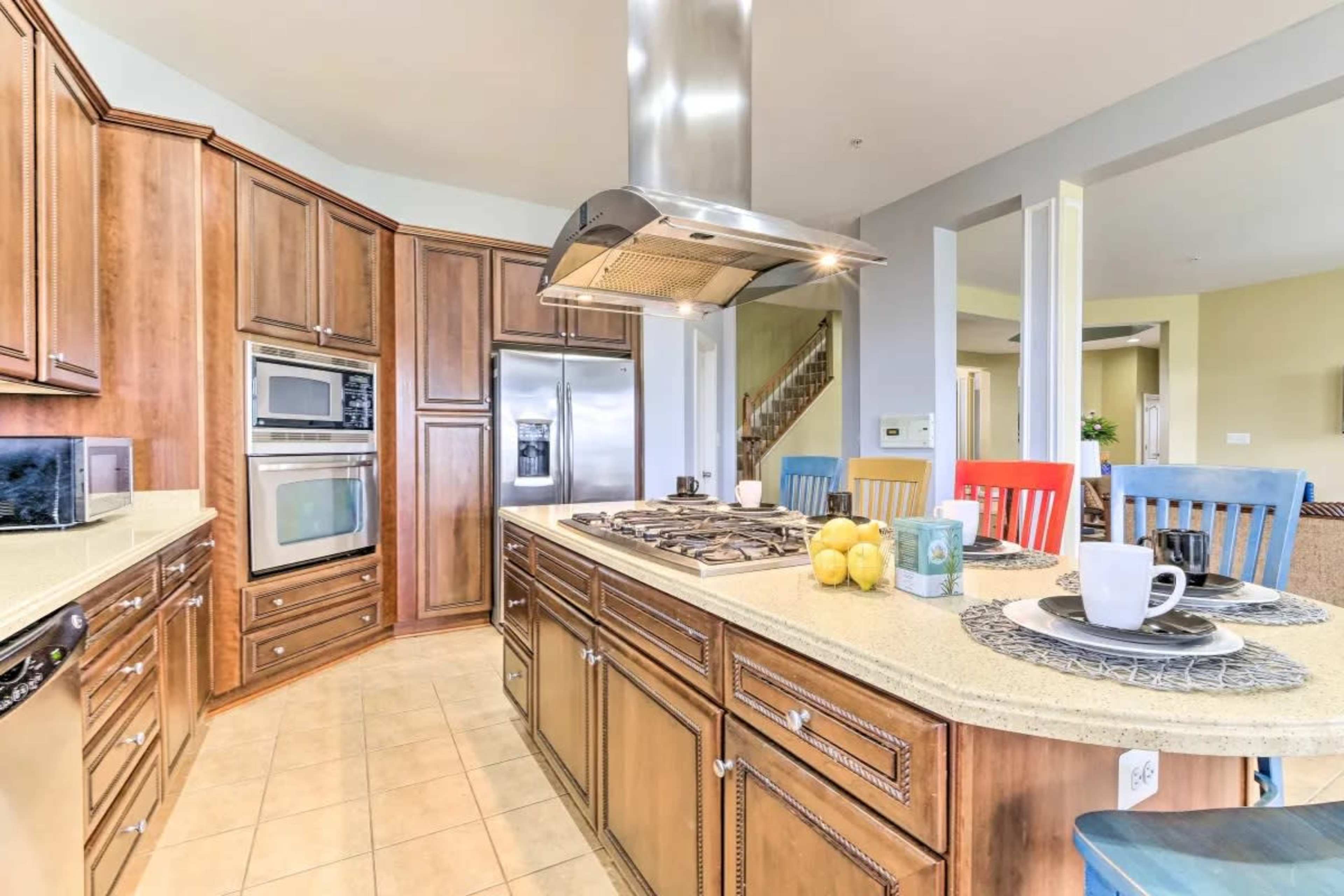 The kitchen features wooden cabinetry, a large island with a stovetop, and colorful chairs around the dining area.