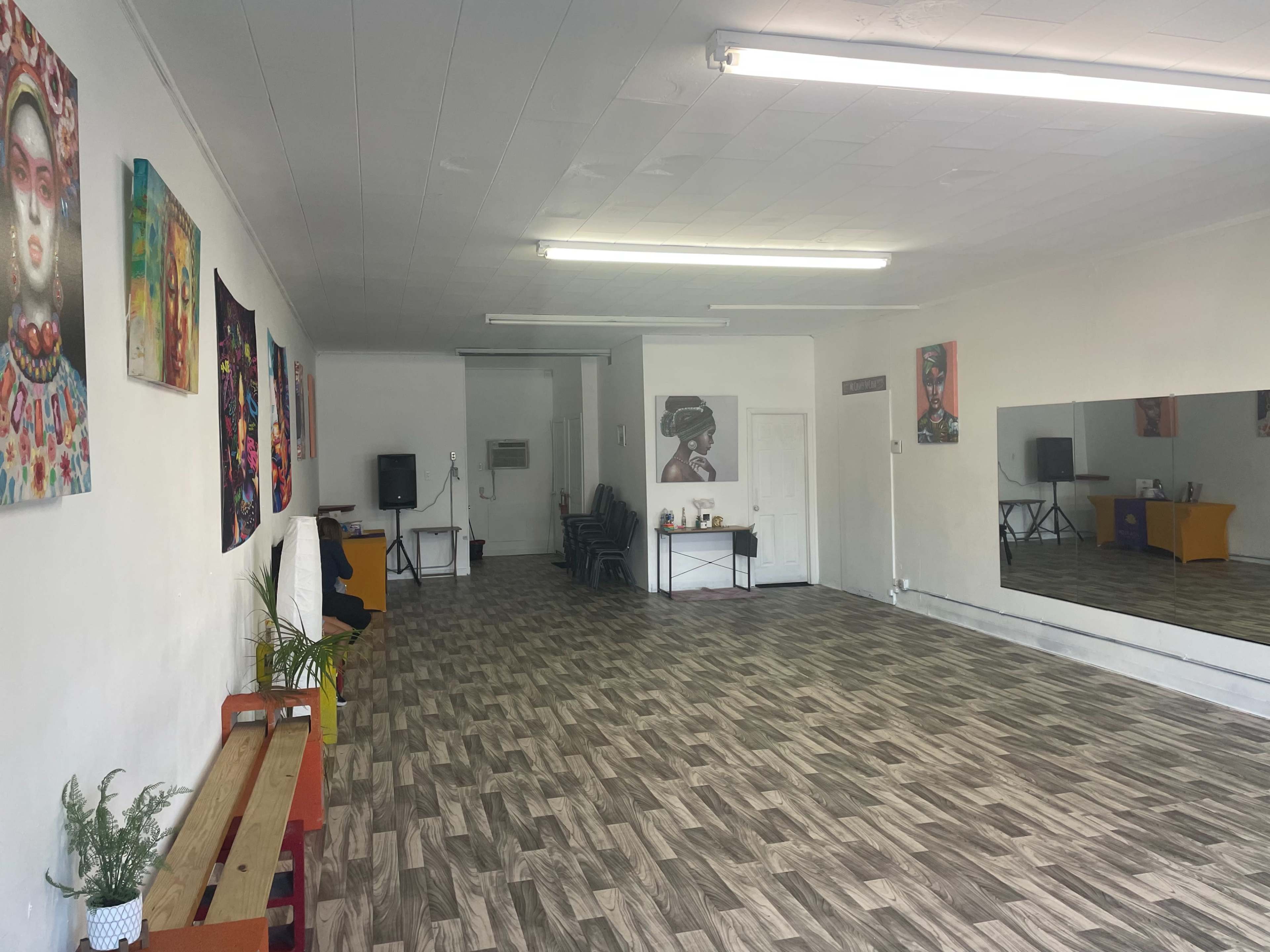 A spacious, well-lit room with a wooden floor, adorned with vibrant wall art, and featuring a large mirror on one side.