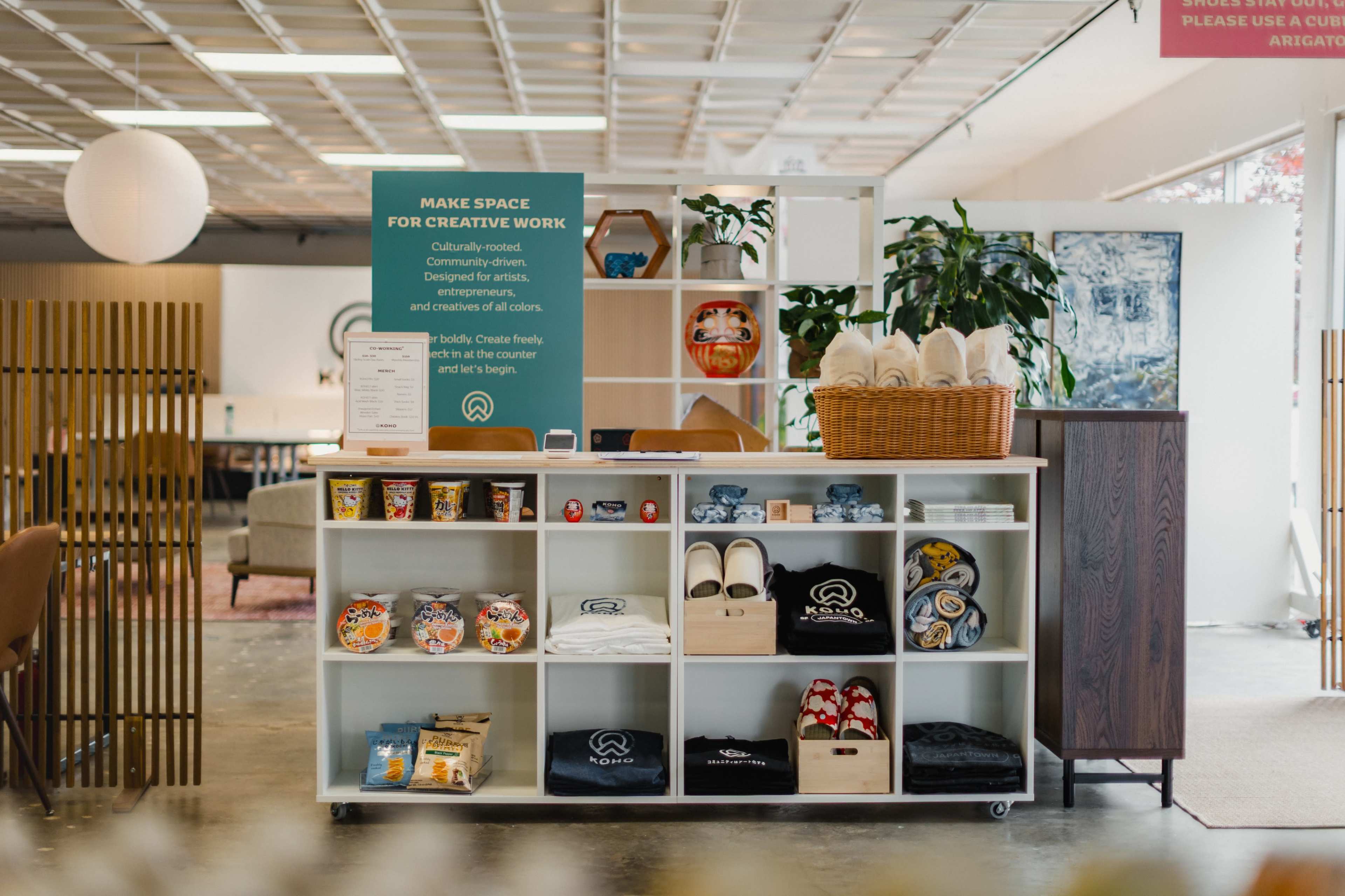 The image shows a well-organized display shelf in a creative workspace featuring various items such as towels, snacks, and branded merchandise.