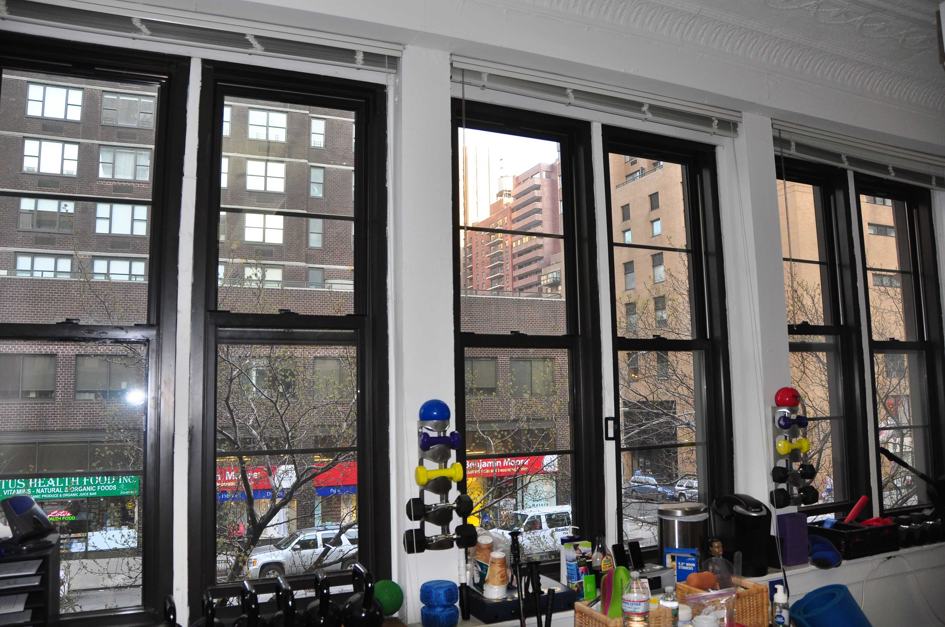 A row of large windows revealing a city street with buildings and parked cars outside.