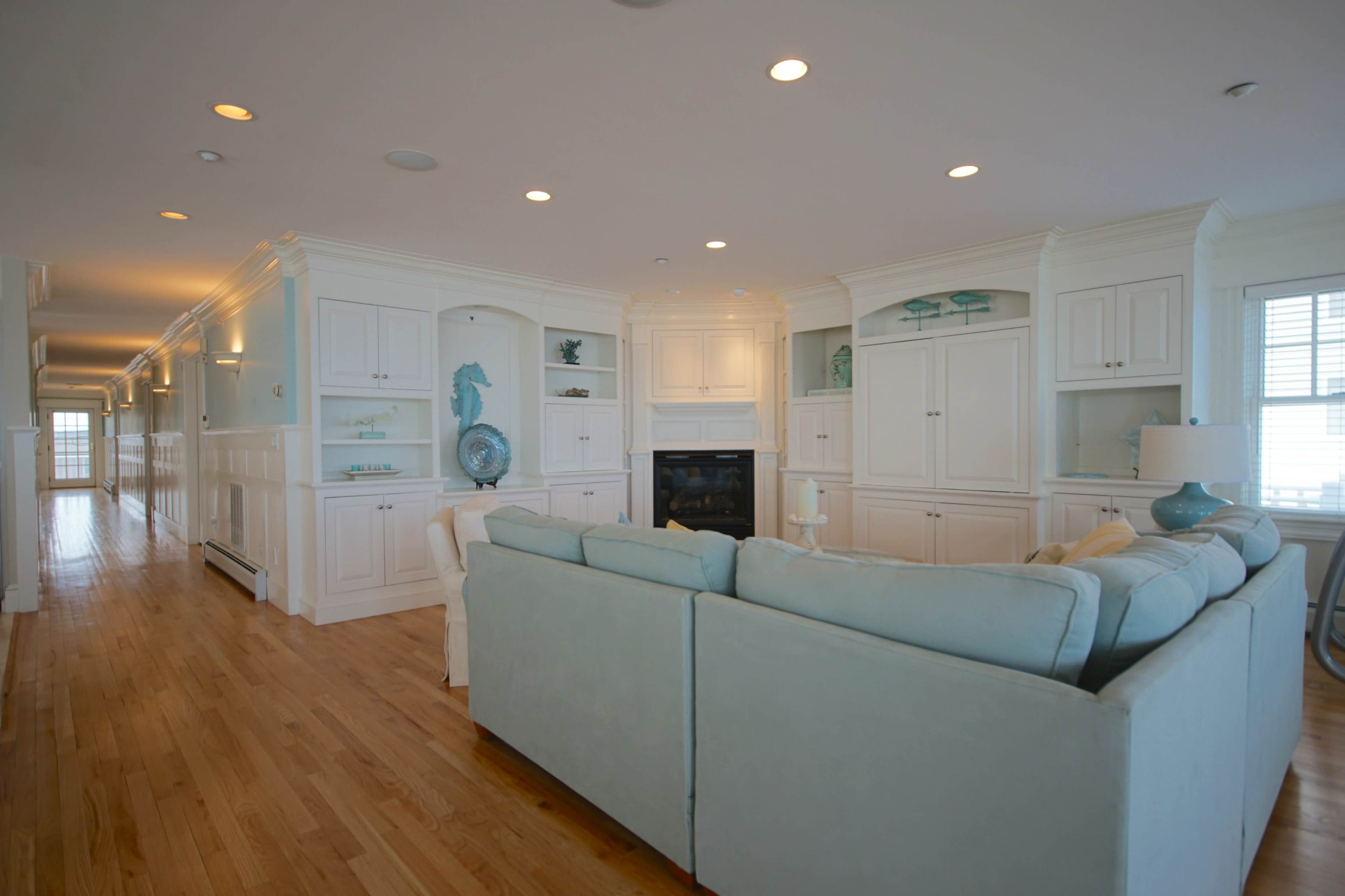 A spacious, well-lit living room with light blue furnishings, white built-in cabinetry, and hardwood flooring.