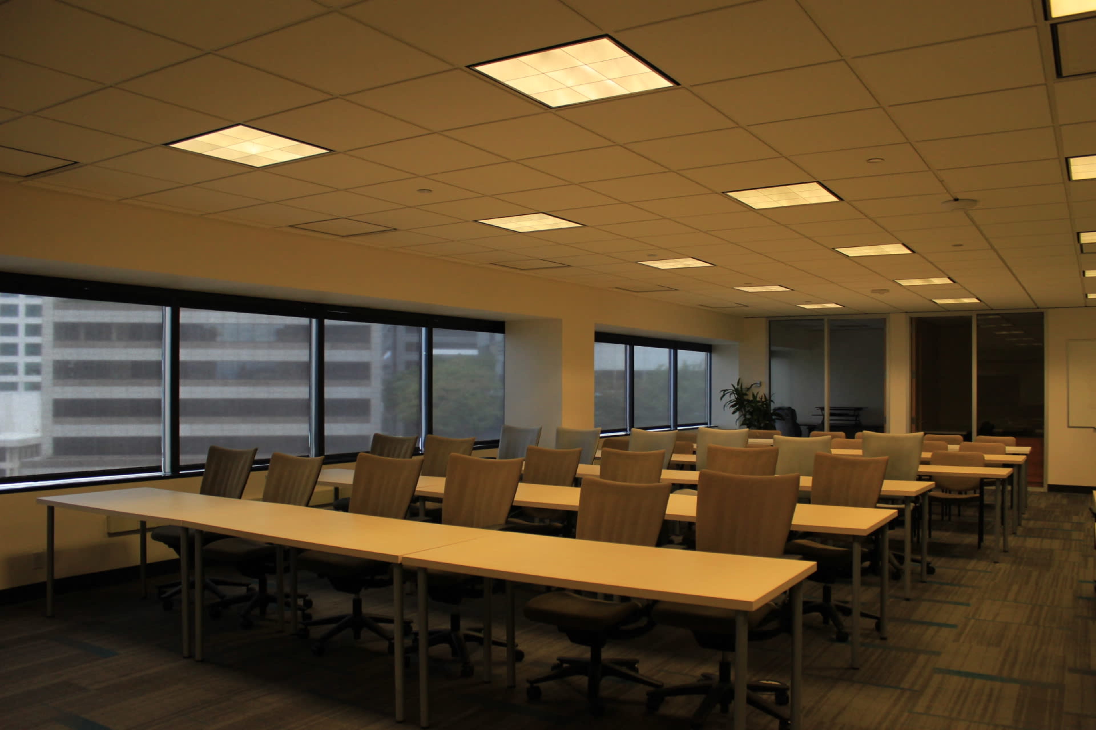 A spacious office conference room with multiple long tables and rows of chairs facing large windows.