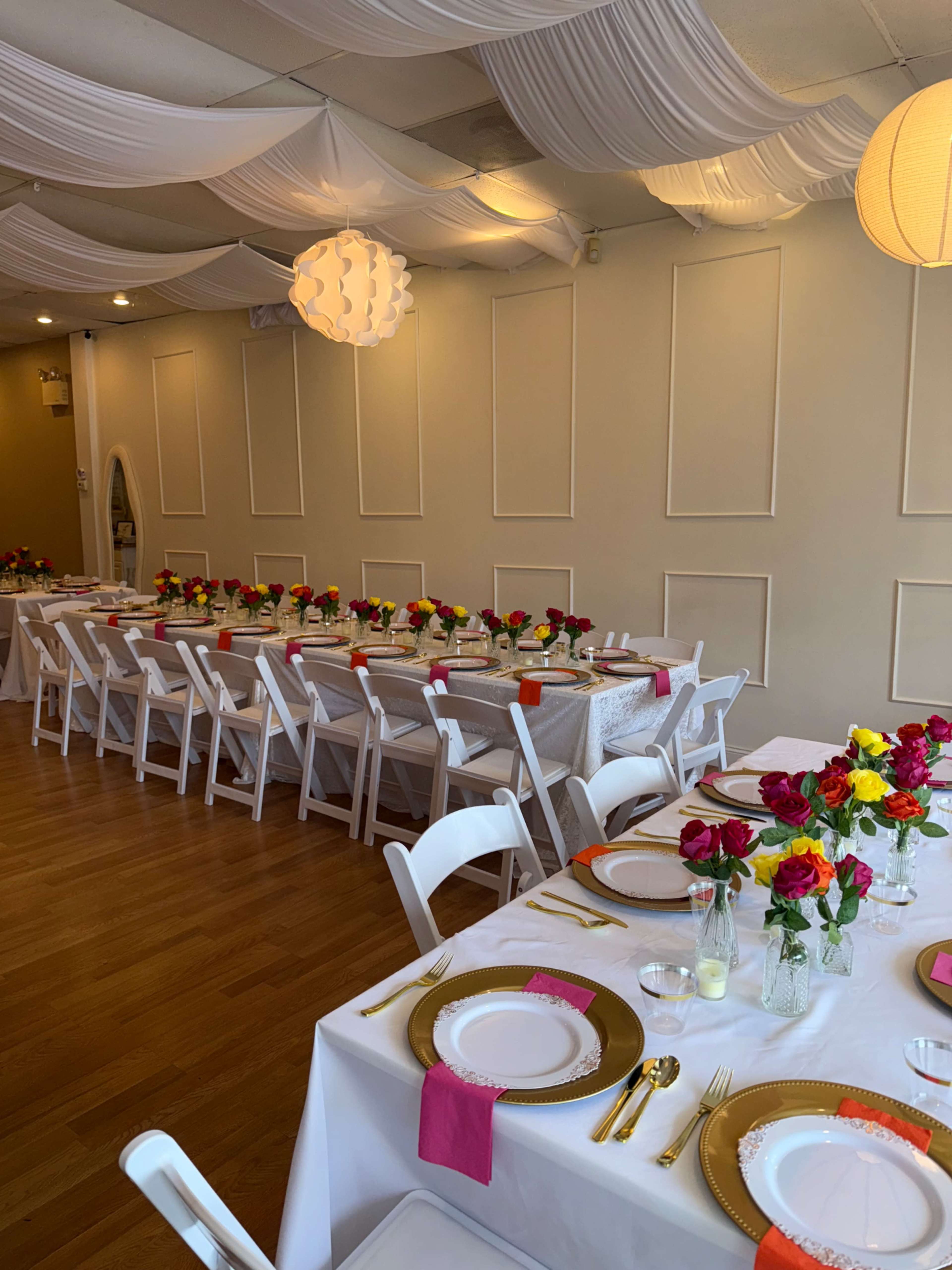 A banquet hall is set up with elegantly arranged tables adorned with colorful flower centerpieces and gold-accented tableware.