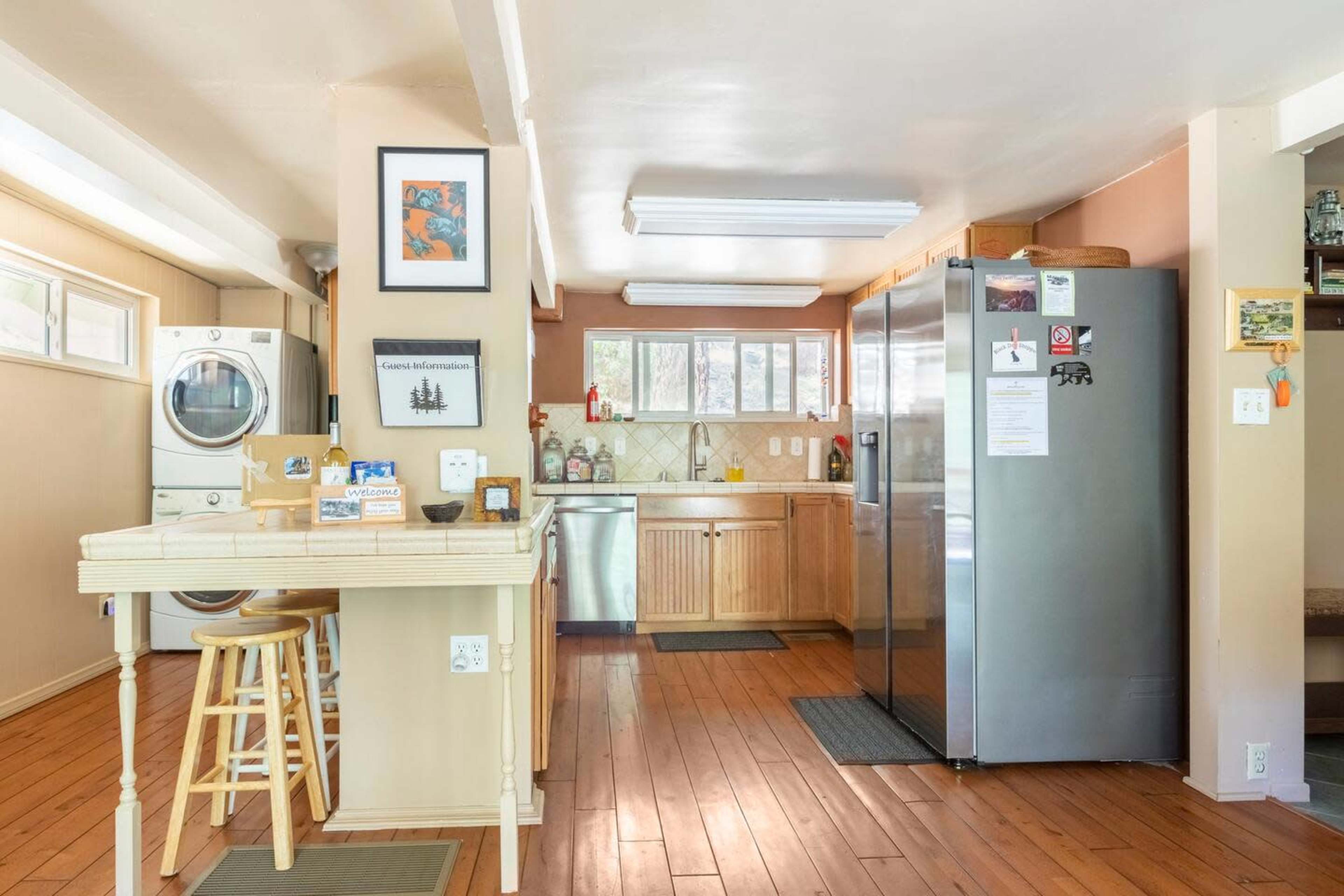 A kitchen with wooden cabinetry, stainless steel appliances, a laundry area, and a small wooden table with stools.