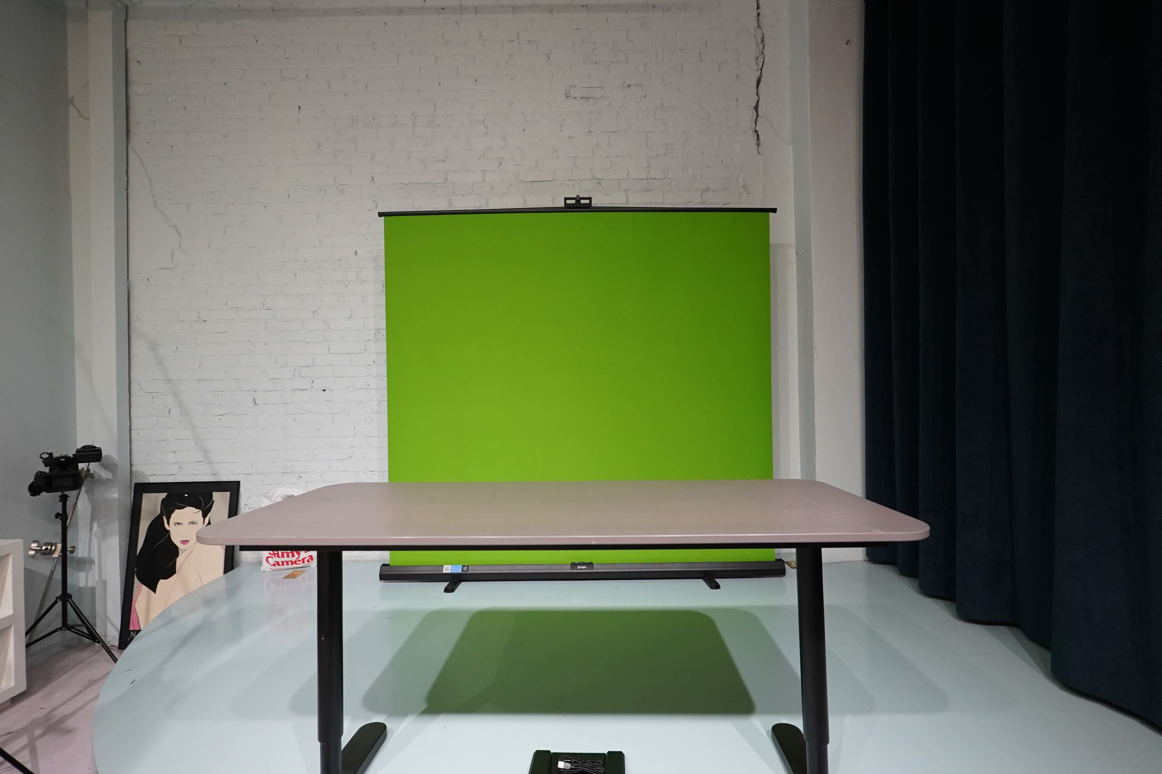 The image shows a studio setup with a green backdrop, a table in the foreground, and a camera positioned to the left.