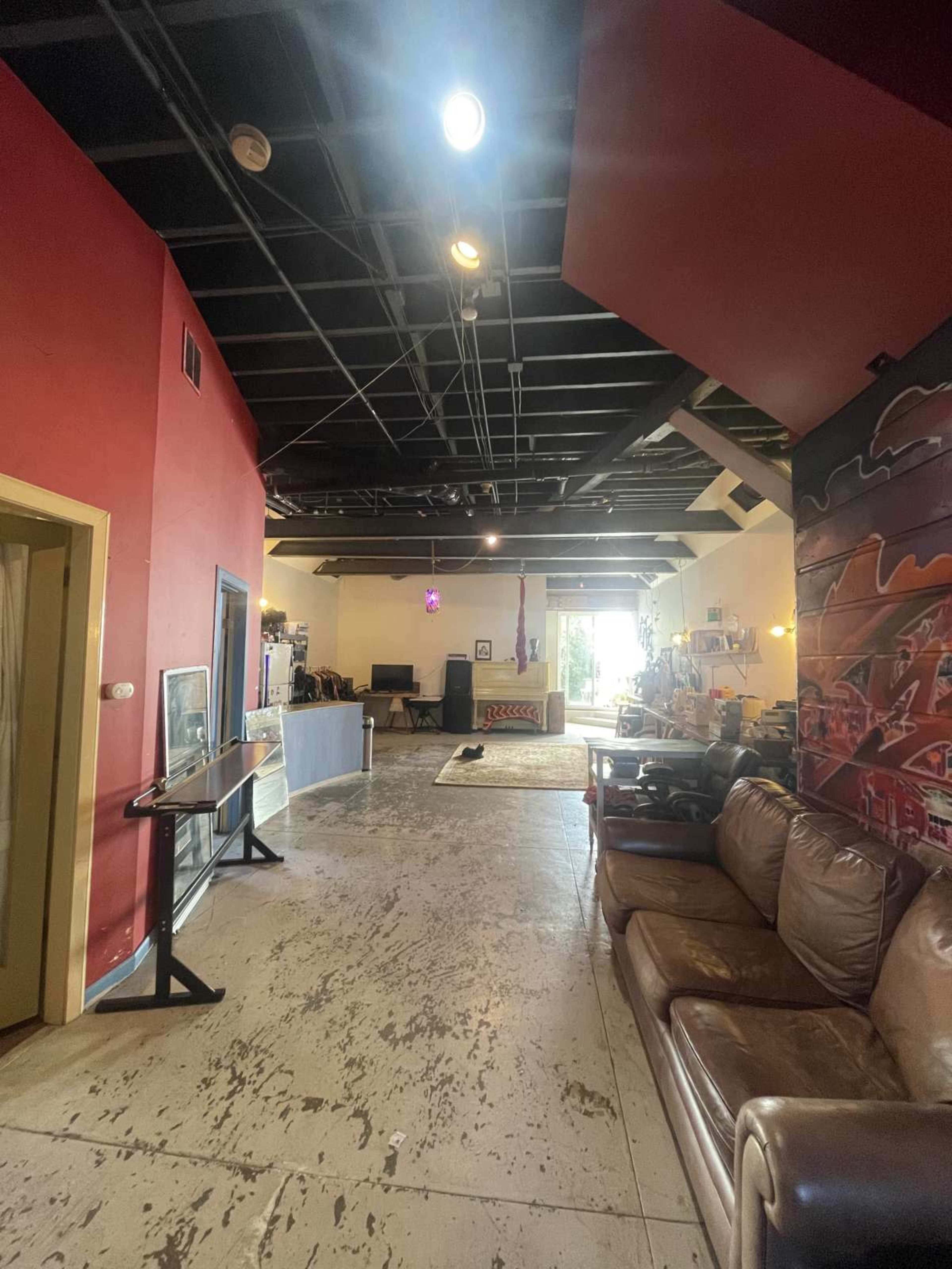 The image shows a spacious interior featuring a combination of red walls and exposed black ceilings, with a living area that includes sofas and various entertainment equipment.