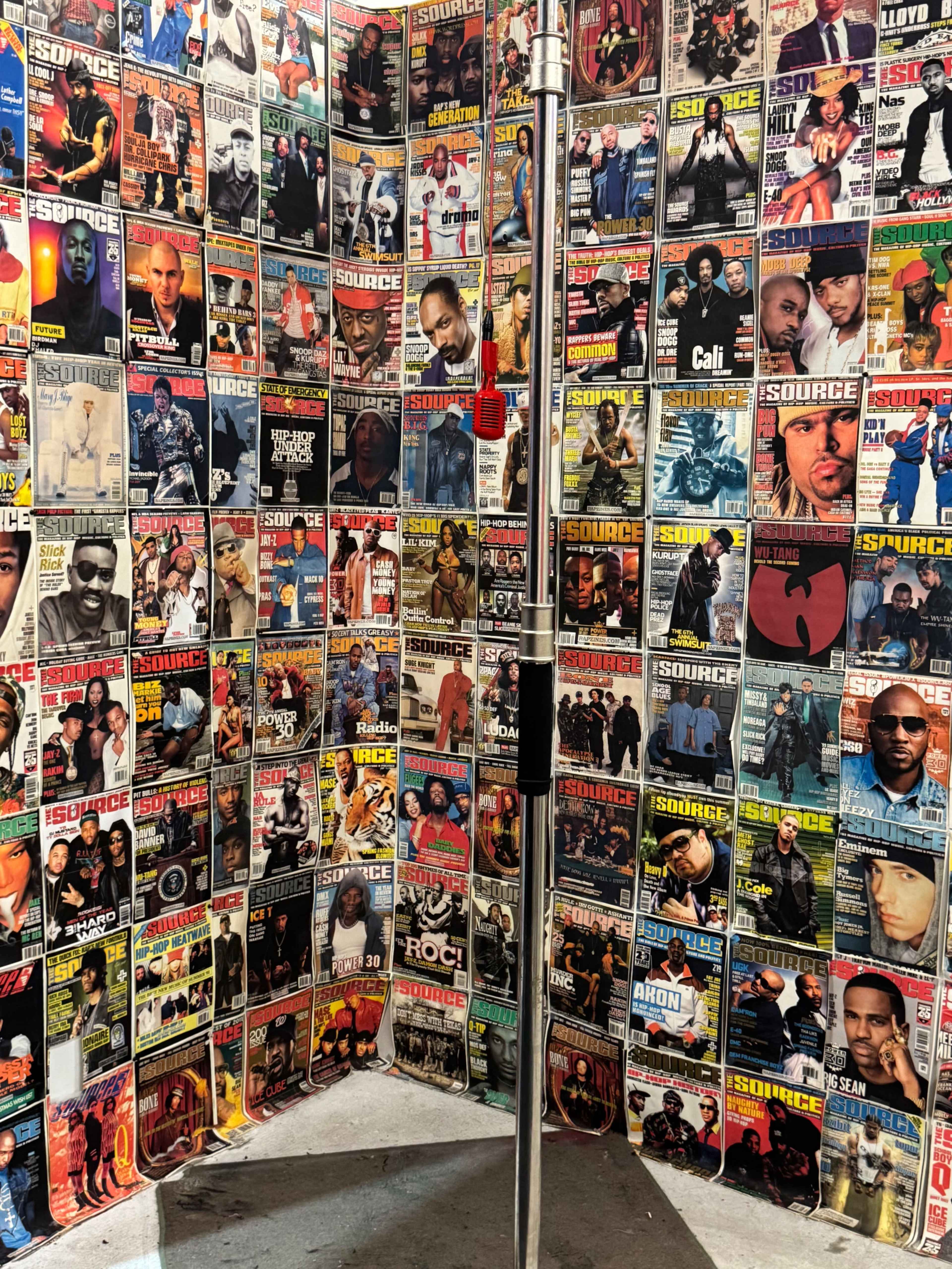 The image shows a wall covered with numerous issues of *The Source* magazine, showcasing various hip-hop artists and music-related themes.