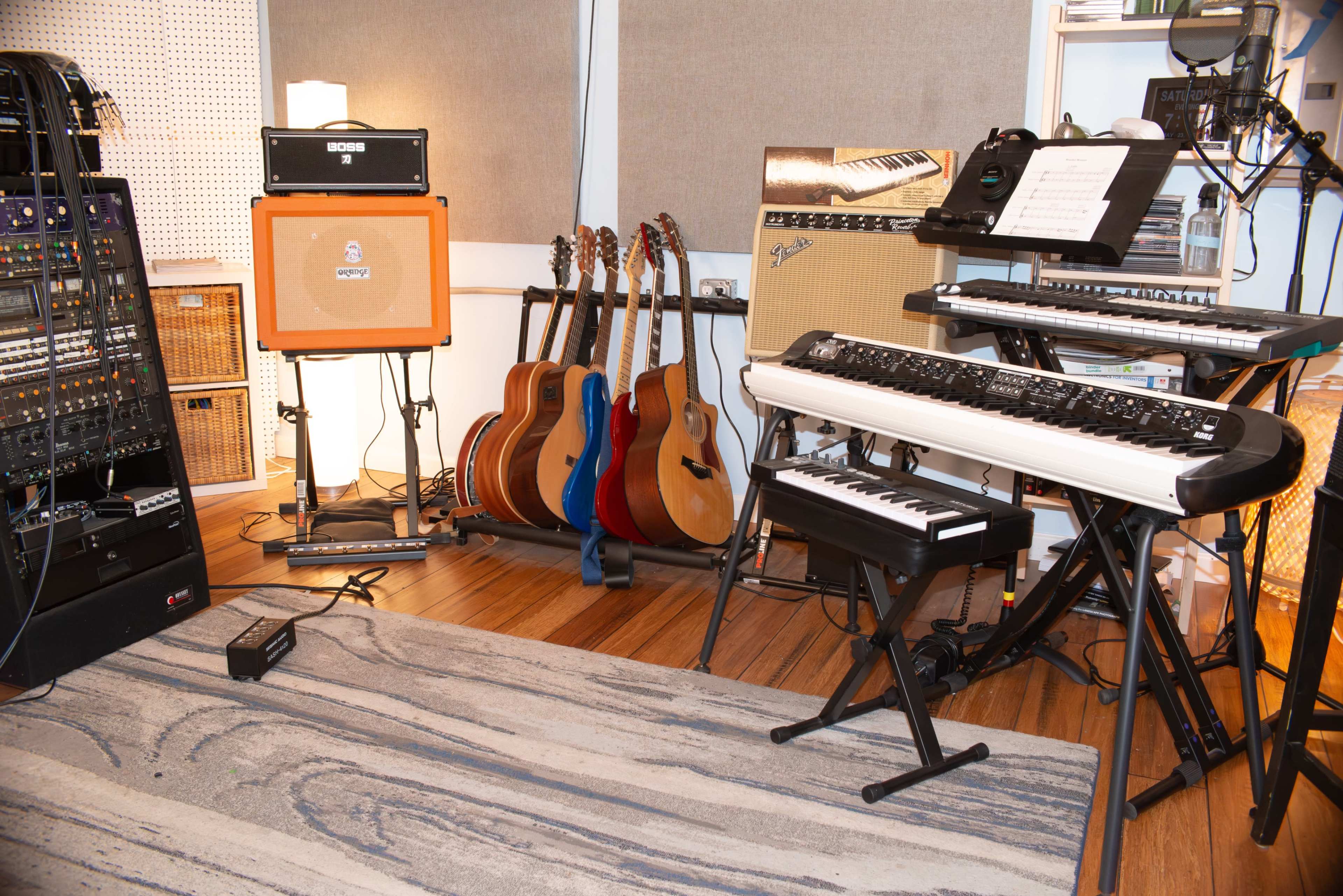 The image shows a music studio setup with various instruments, including electric and acoustic guitars, amplifiers, and keyboards arranged around a carpeted floor.