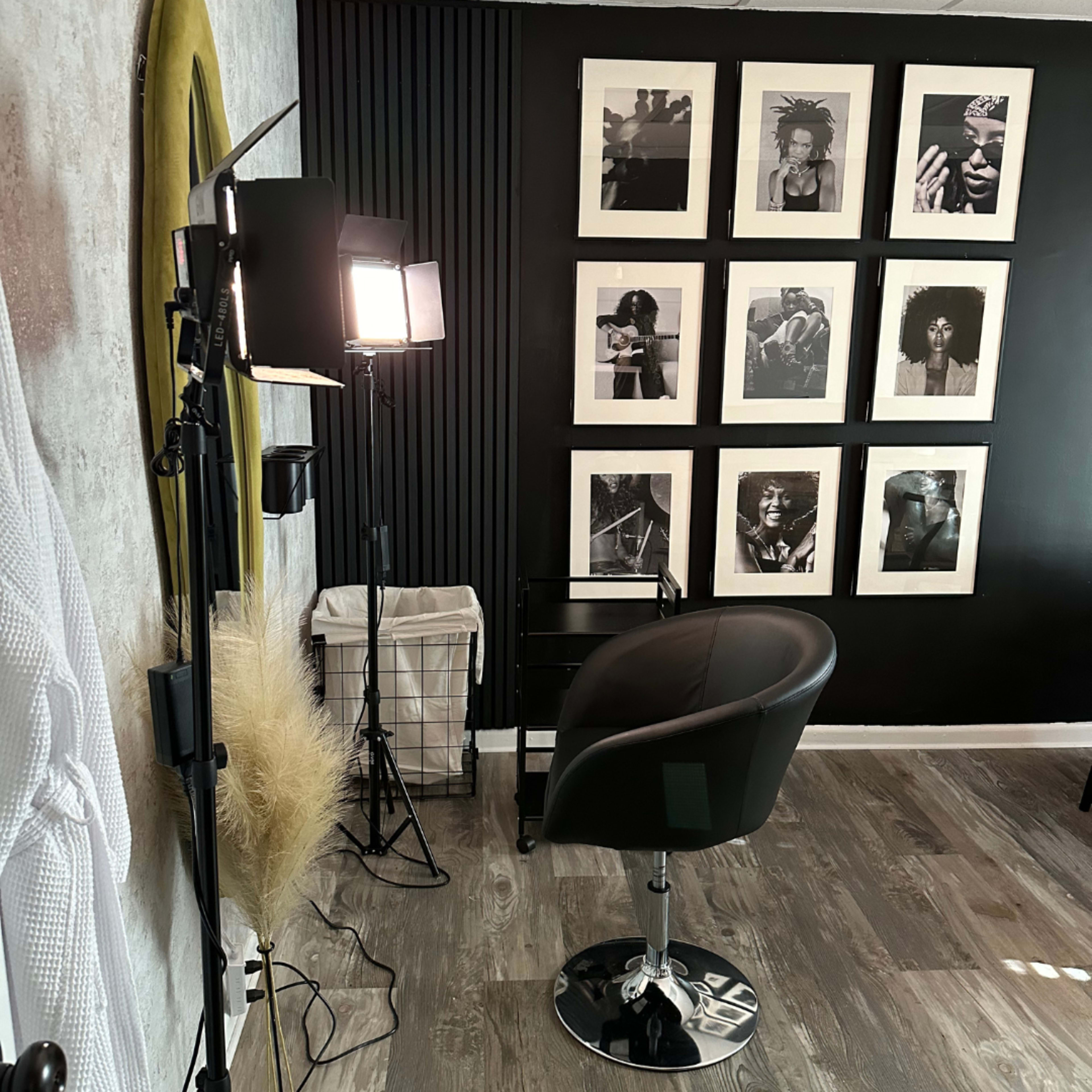 A hair salon interior featuring a black chair positioned in front of a wall adorned with framed black-and-white photographs.