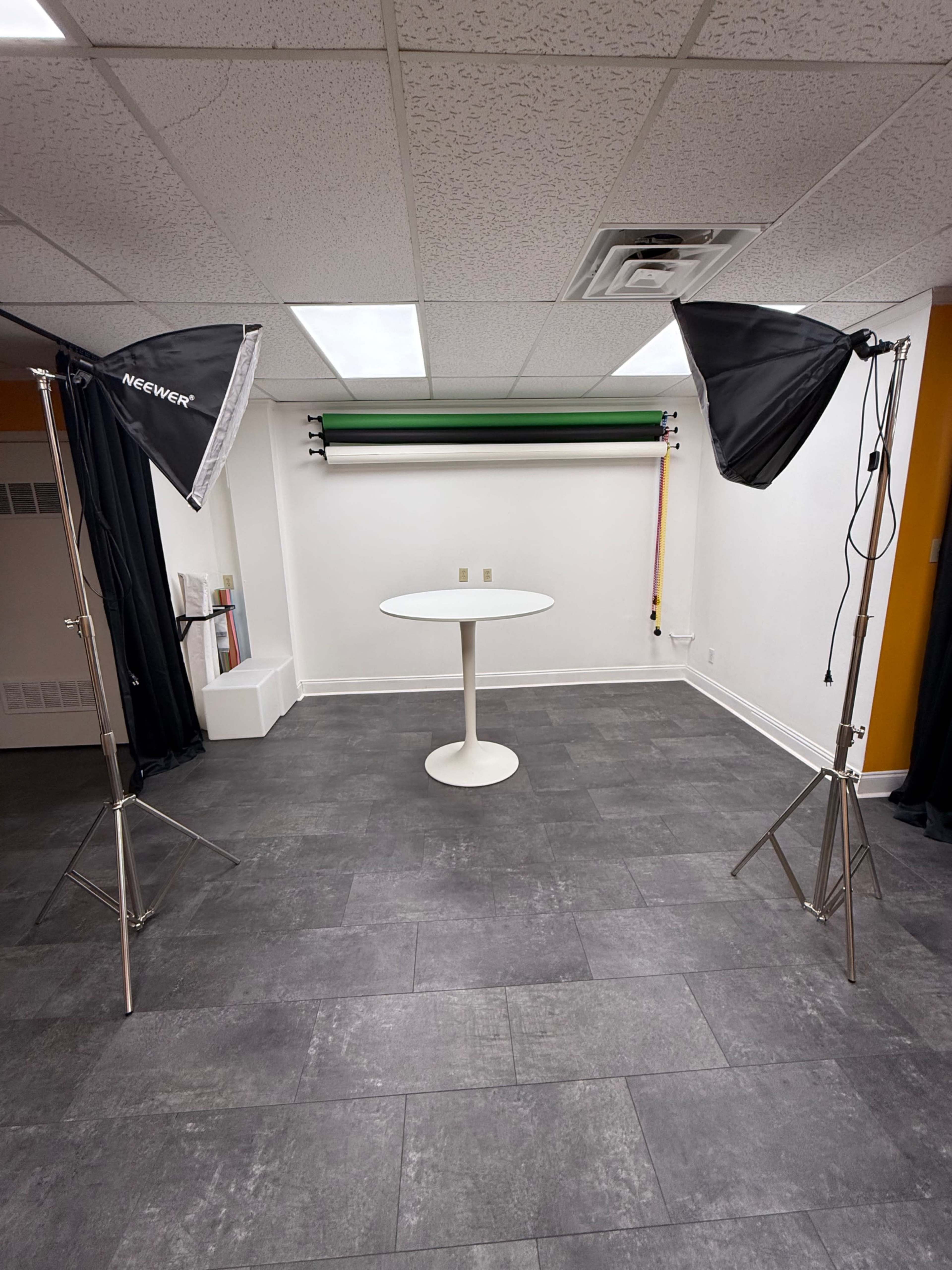 The image shows a photography studio with a round table in the center and two tall light stands with softboxes positioned on either side.