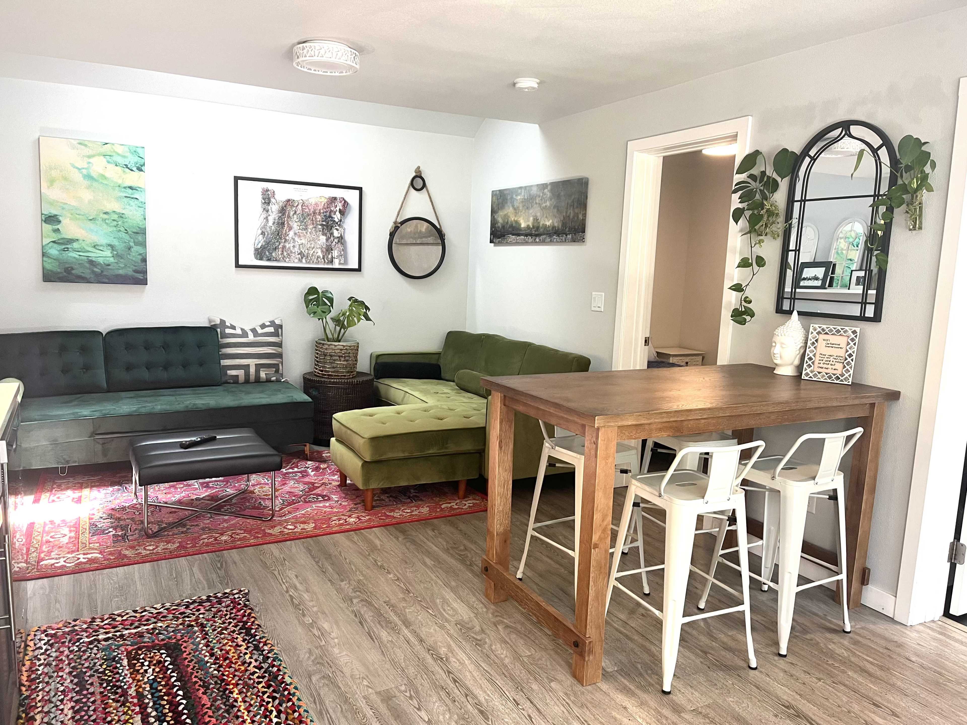 A cozy living area with two green sofas, a wooden dining table with white chairs, and various artworks on the walls.