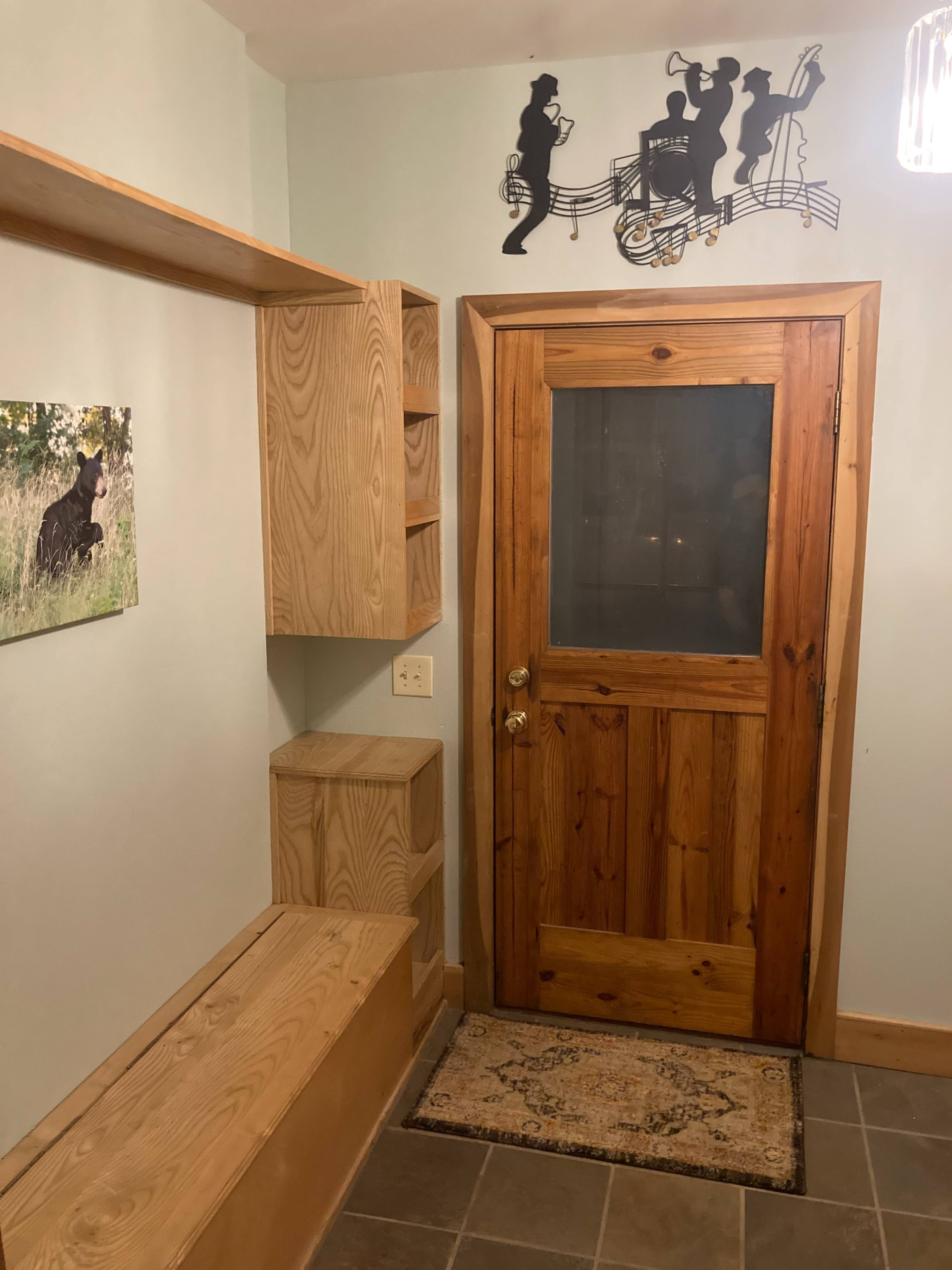 A wooden entryway with a door, built-in shelves, a bench, and a decorative musical silhouette mounted on the wall.