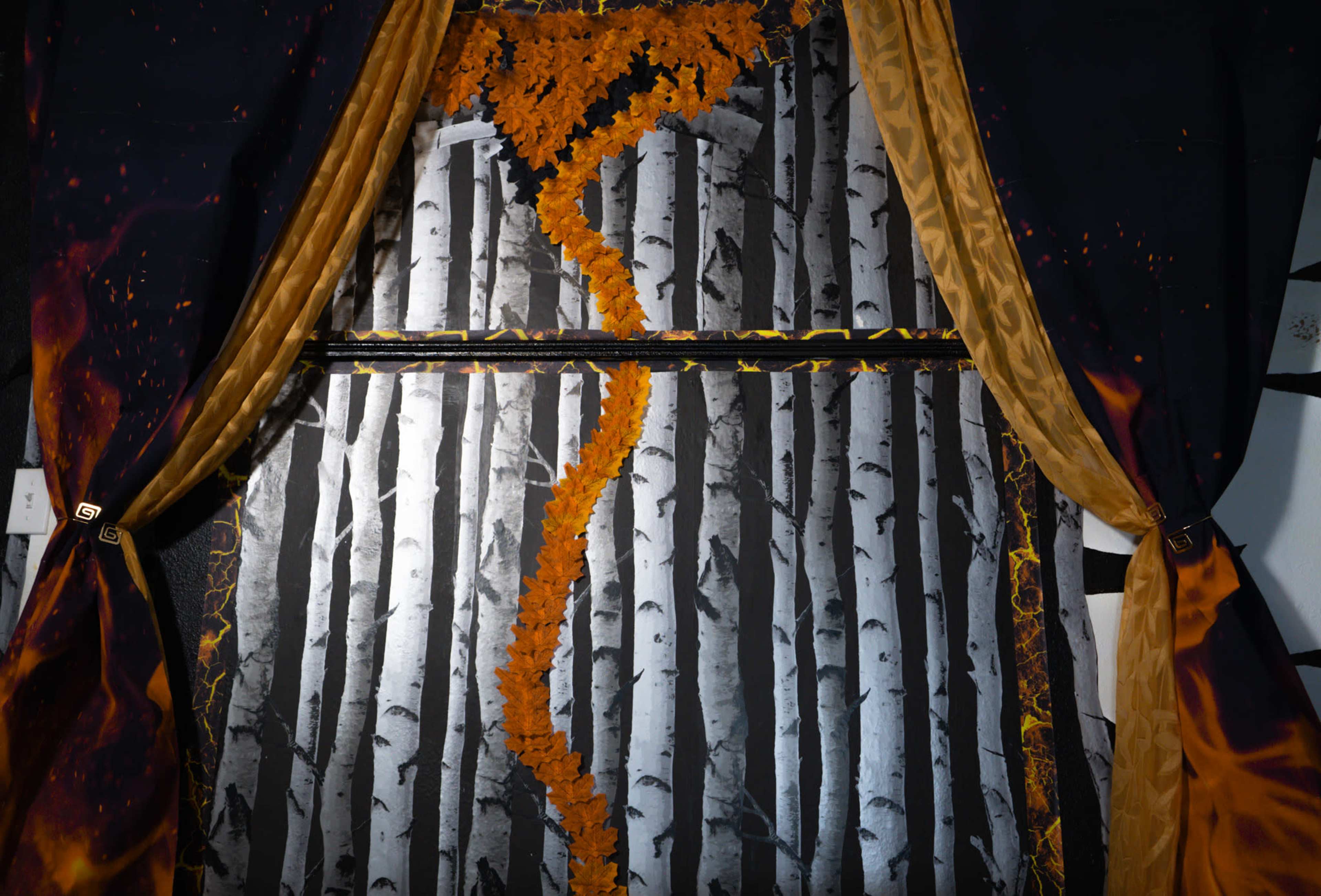 The image features a backdrop of black and white birch trees with a decorative orange leaf garland running down the center, framed by dark curtains.