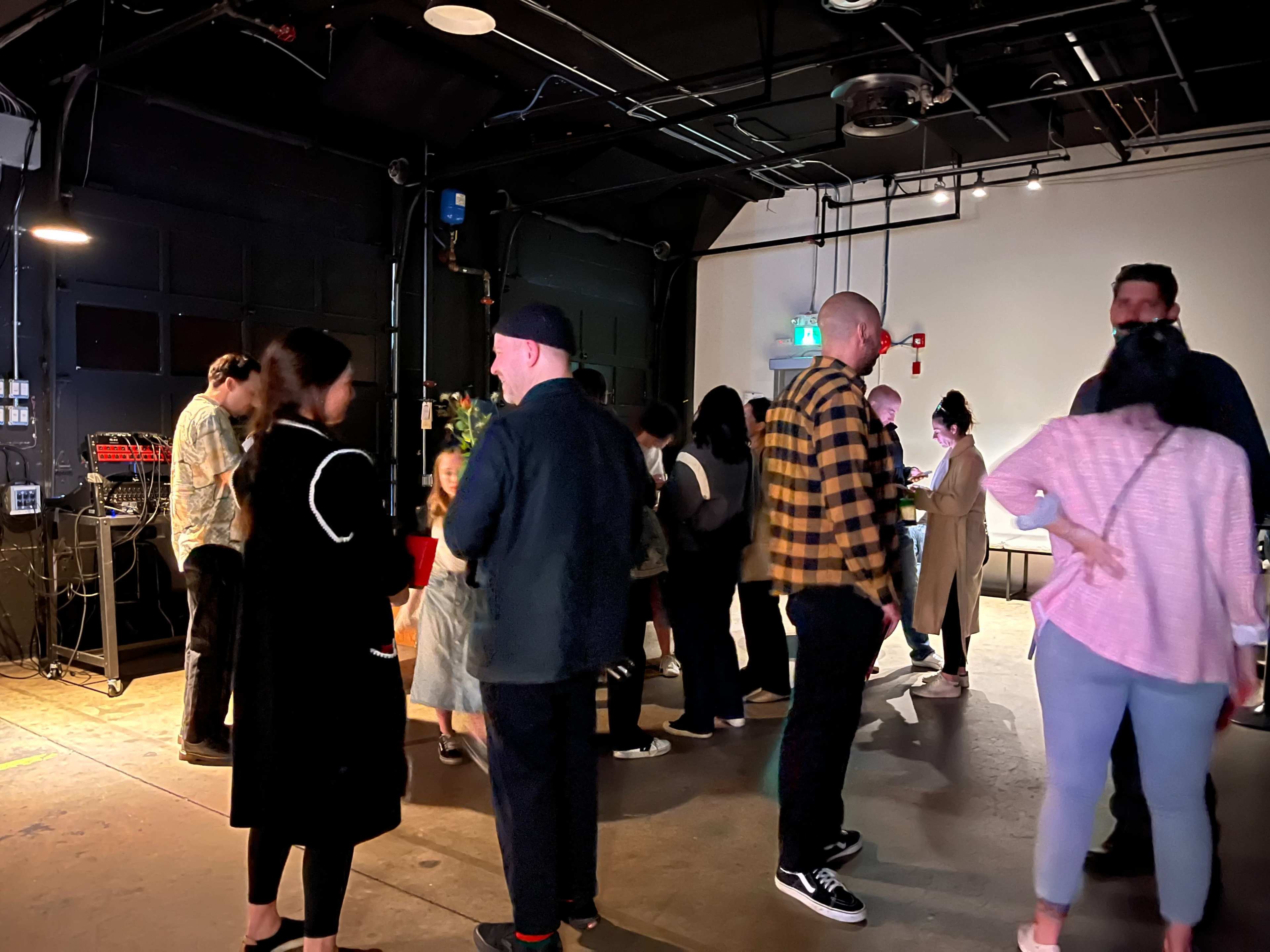 A group of people socialize in a dimly lit indoor space, with music equipment and decorations in the background.