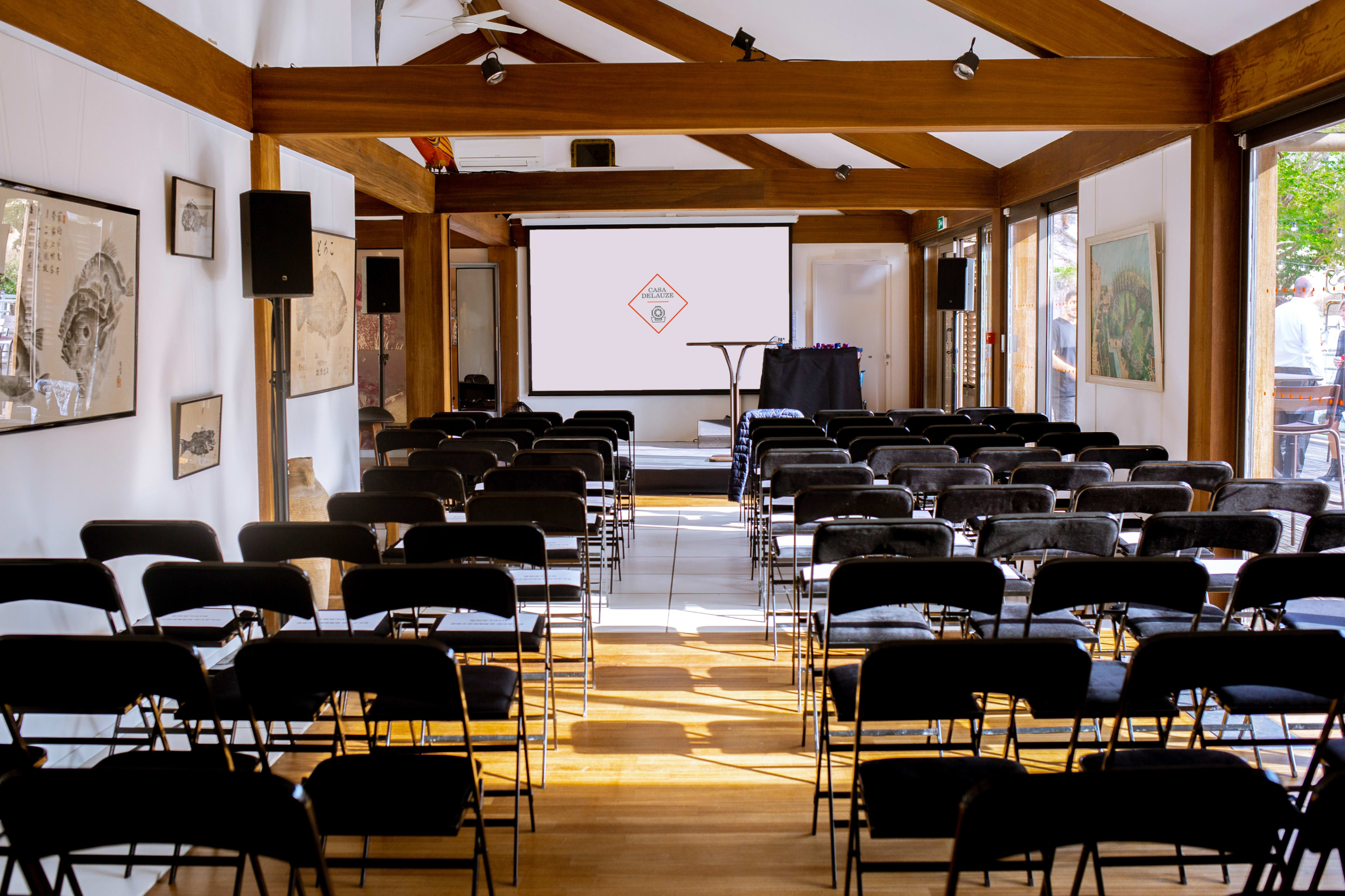 The image shows an empty conference room set up with rows of black chairs facing a presentation screen at the front.