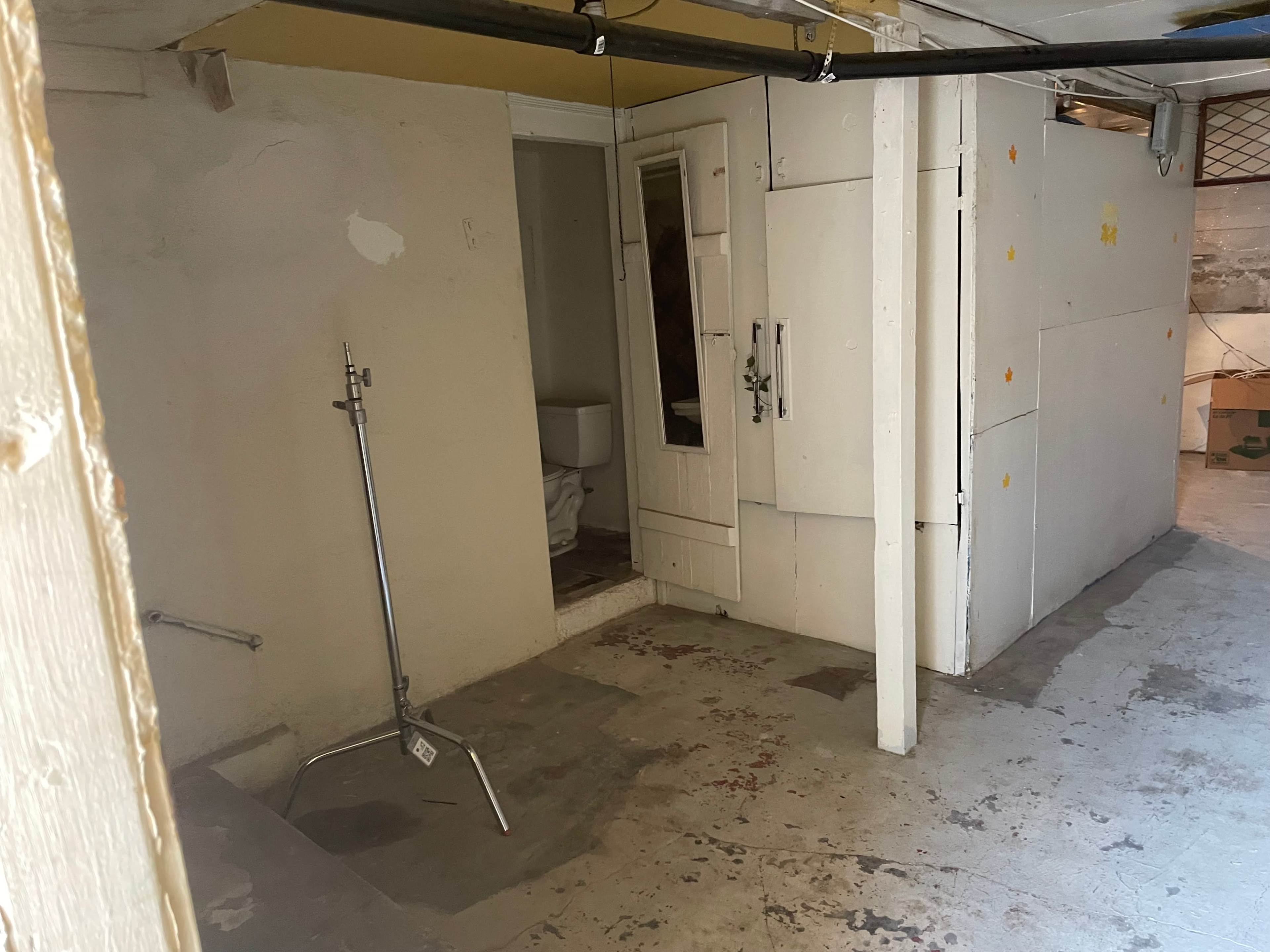 The image shows a bare basement area with a visible entryway to a bathroom and a freestanding metal clothing rack.