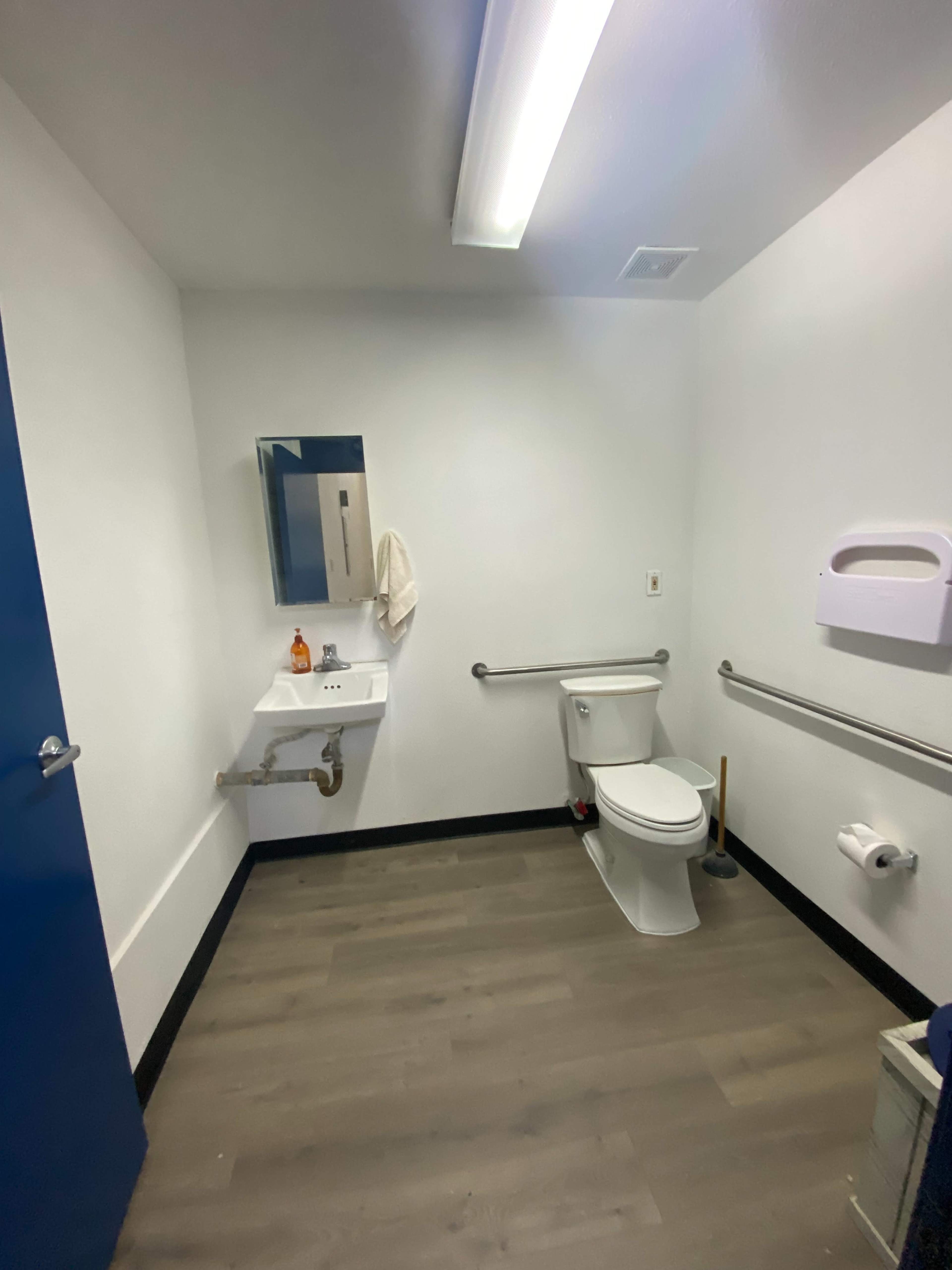 A clean, minimally furnished restroom with a toilet, sink, and a mirror on the wall.