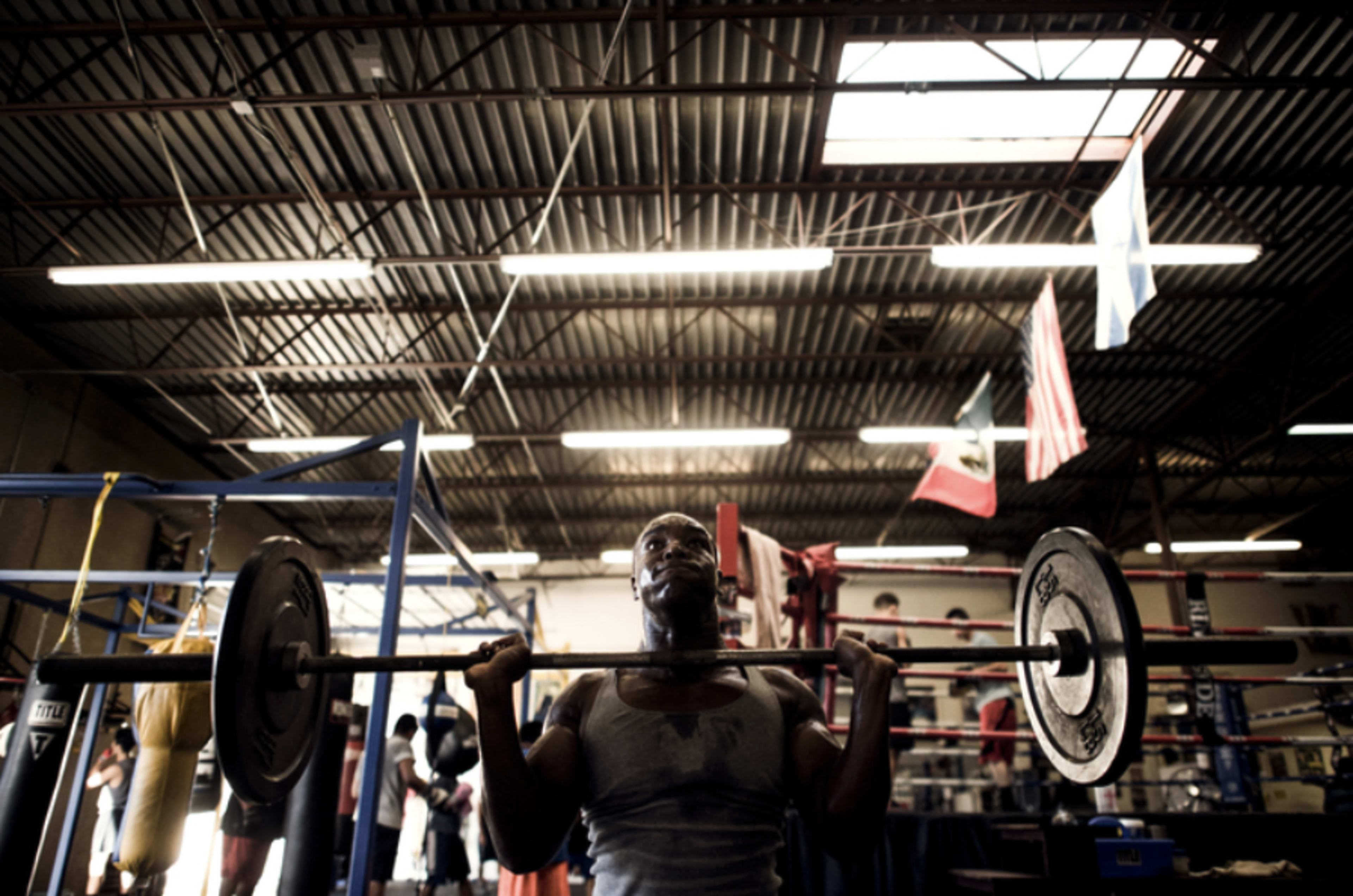 A person lifts a barbell in a weightlifting gym with various flags hanging from the ceiling.