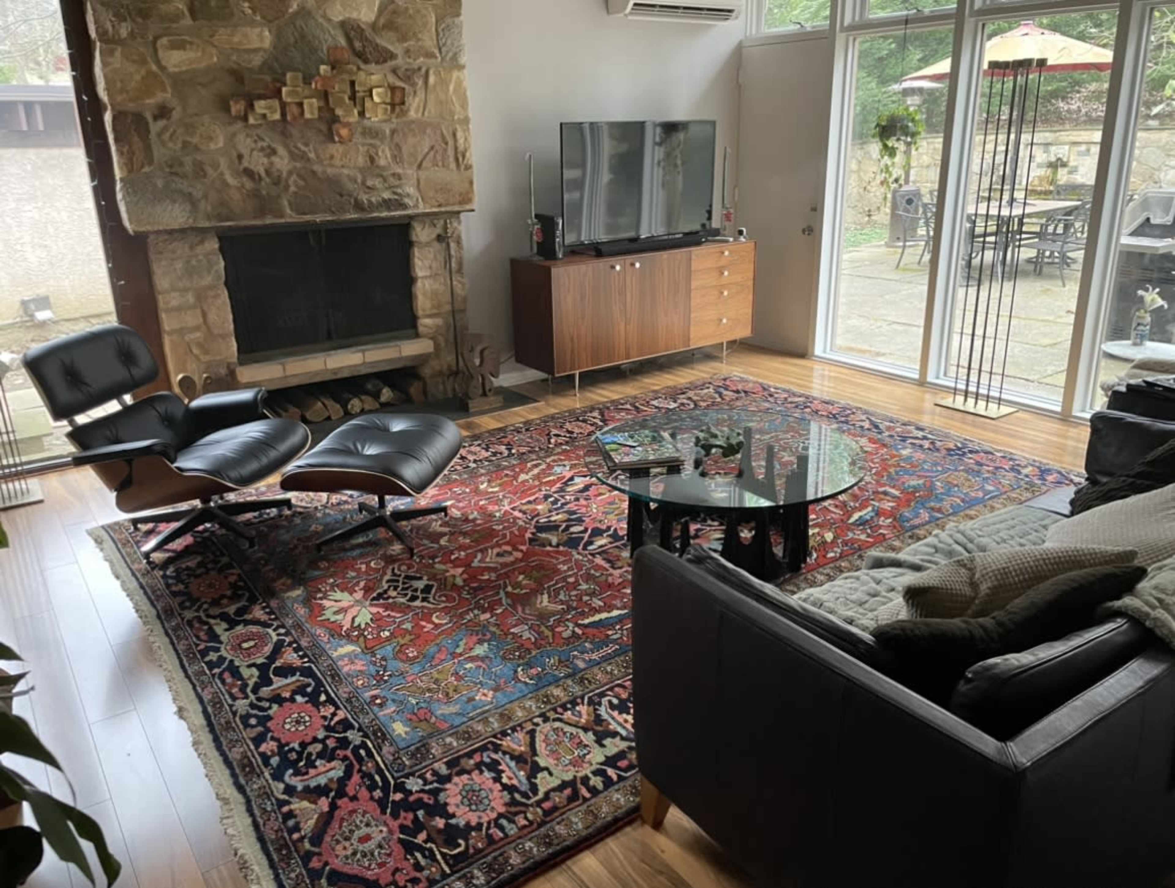 The living room features a stone fireplace, a television on a wooden cabinet, and modern black furniture arranged around a patterned area rug.