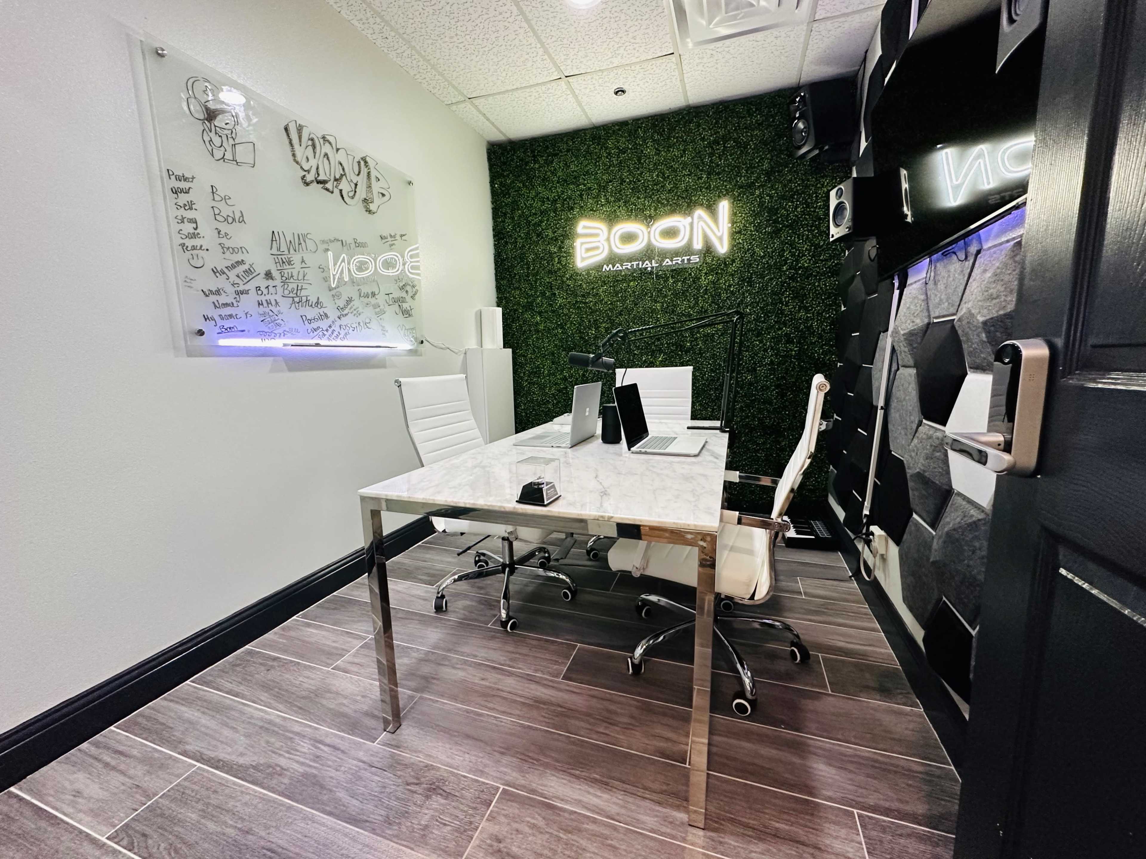 A modern office space featuring a white marble table, two white chairs, a wall with green foliage, and illuminated signage.