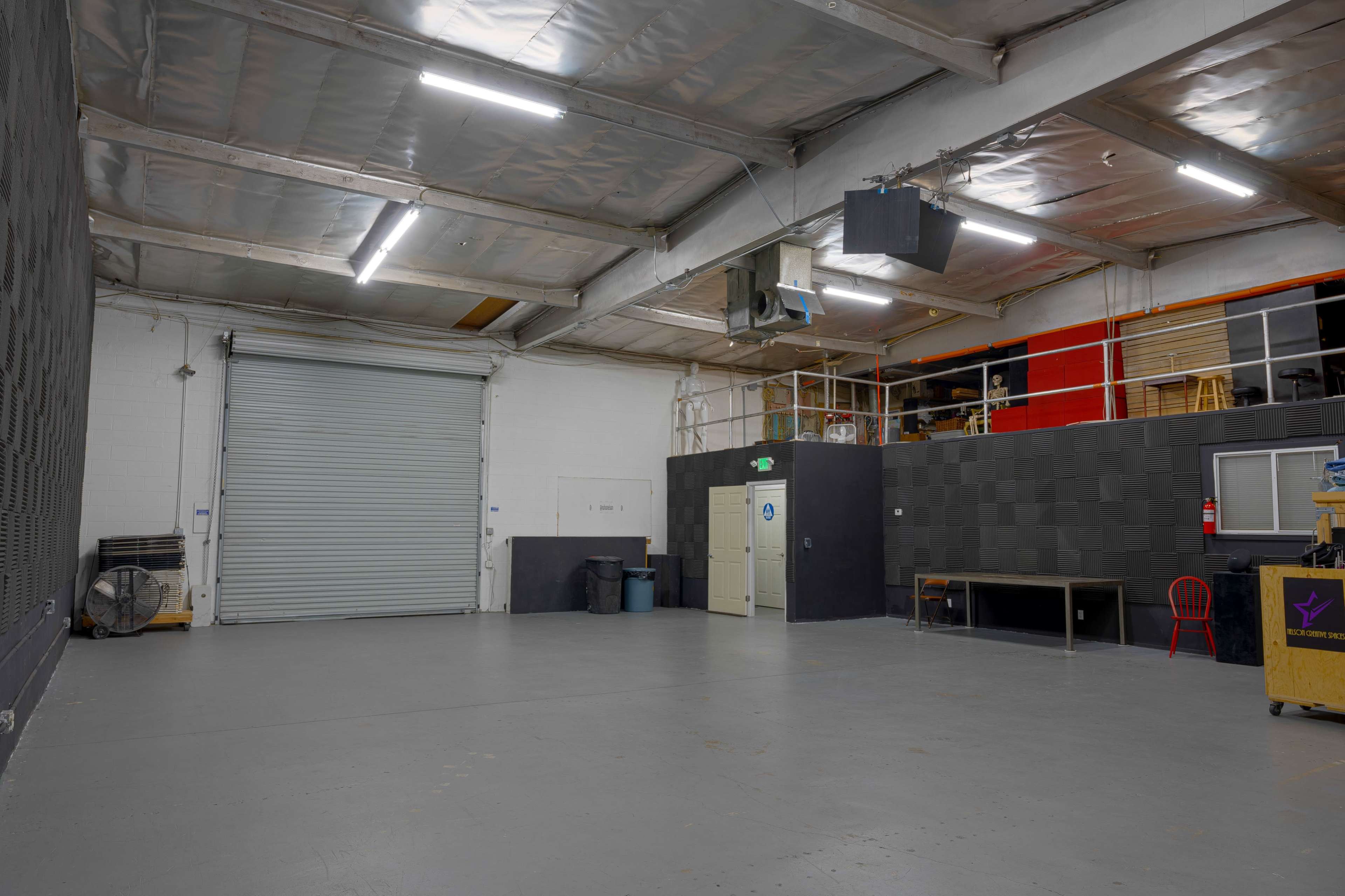 An empty warehouse space with a metallic roll-up door, a small table, and storage areas in the background.