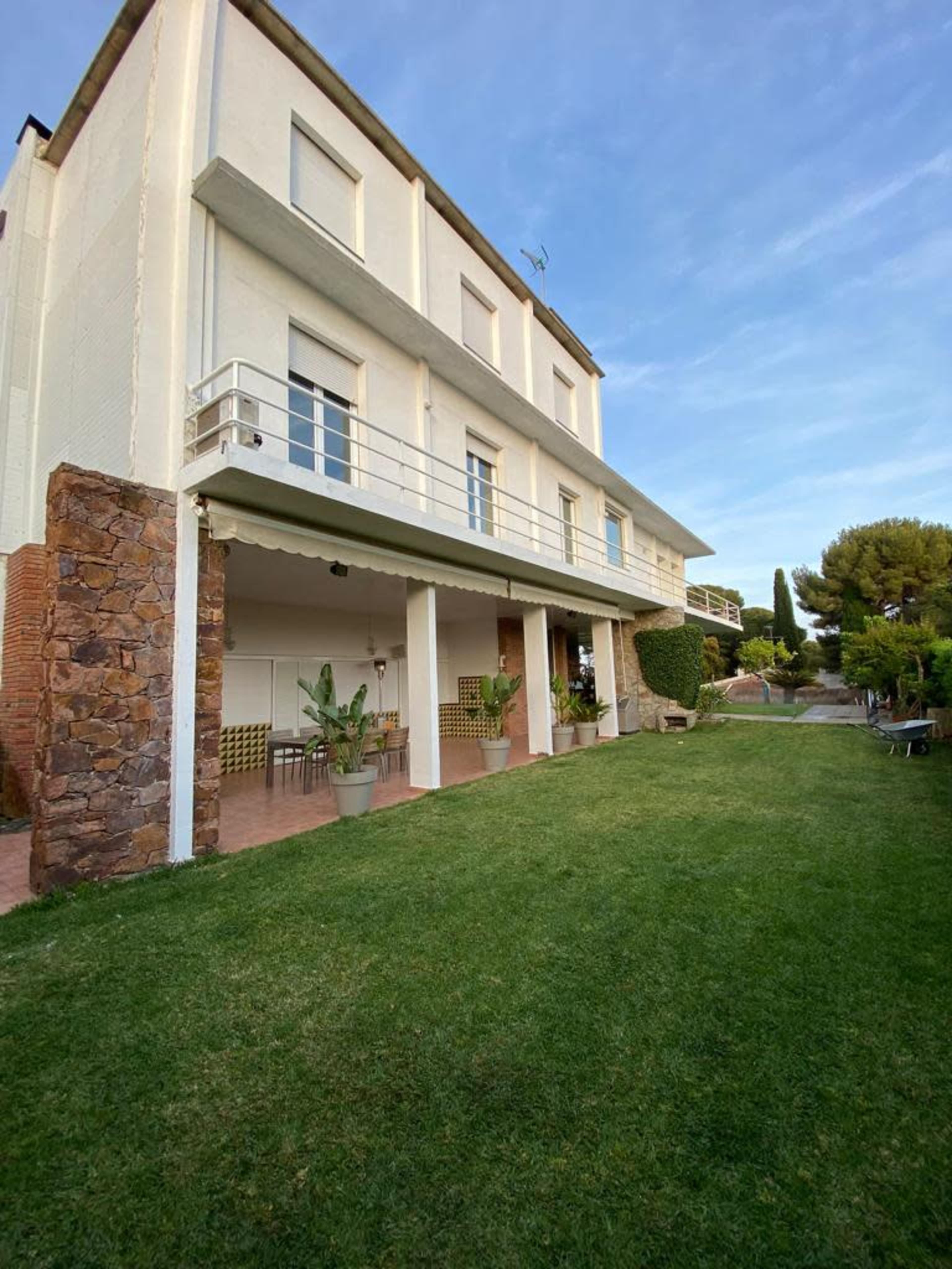 A three-story white building with a stone base and a balcony overlooks a green lawn and landscaped area.