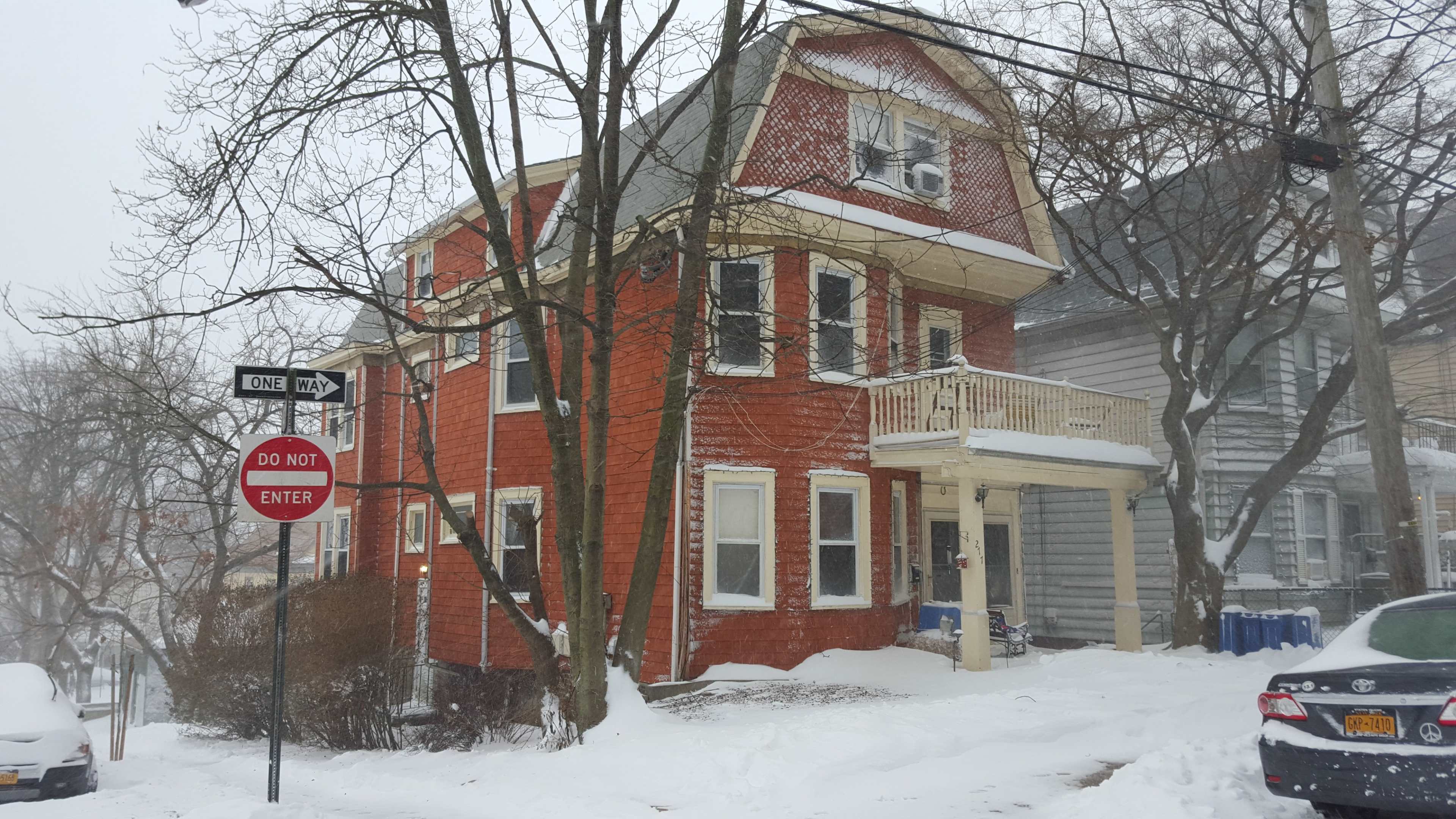 A three-story red house with a balcony sits at the intersection of a snowy street, next to a "Do Not Enter" sign.