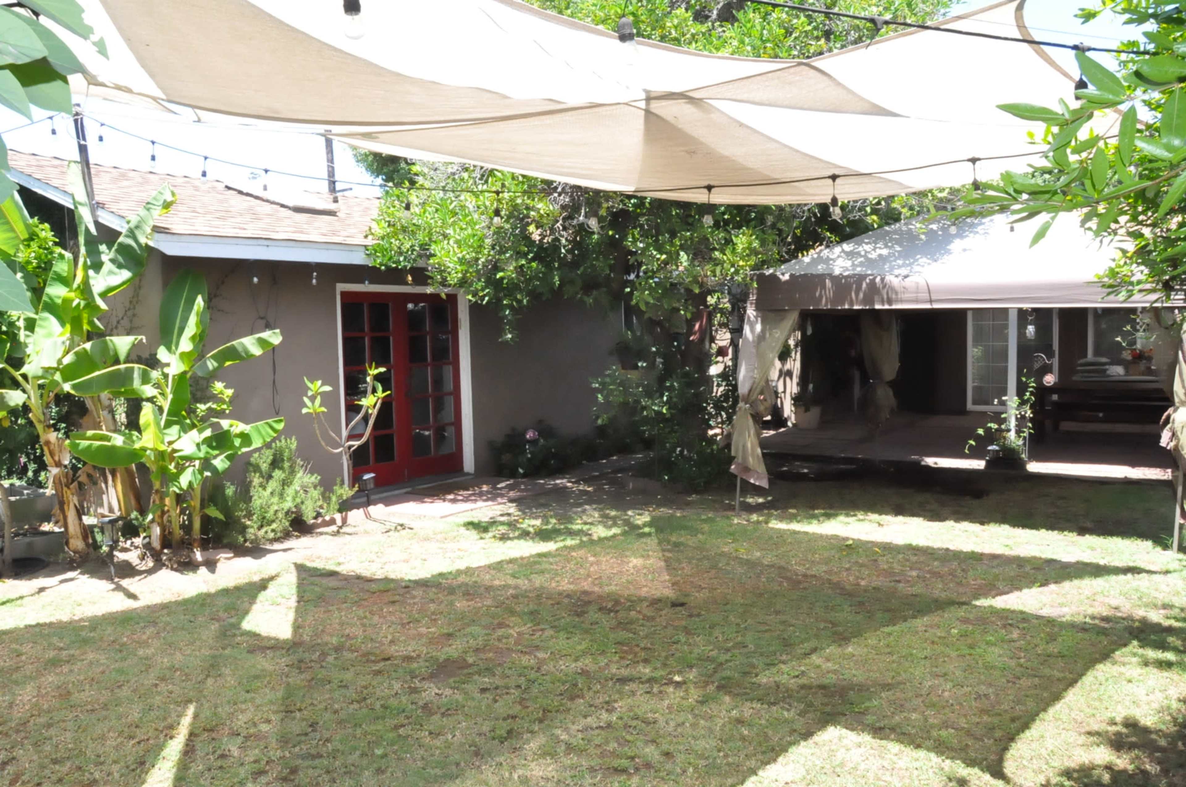 A backyard area with a tent-like structure and a small red door on a house, surrounded by greenery and a lawn.