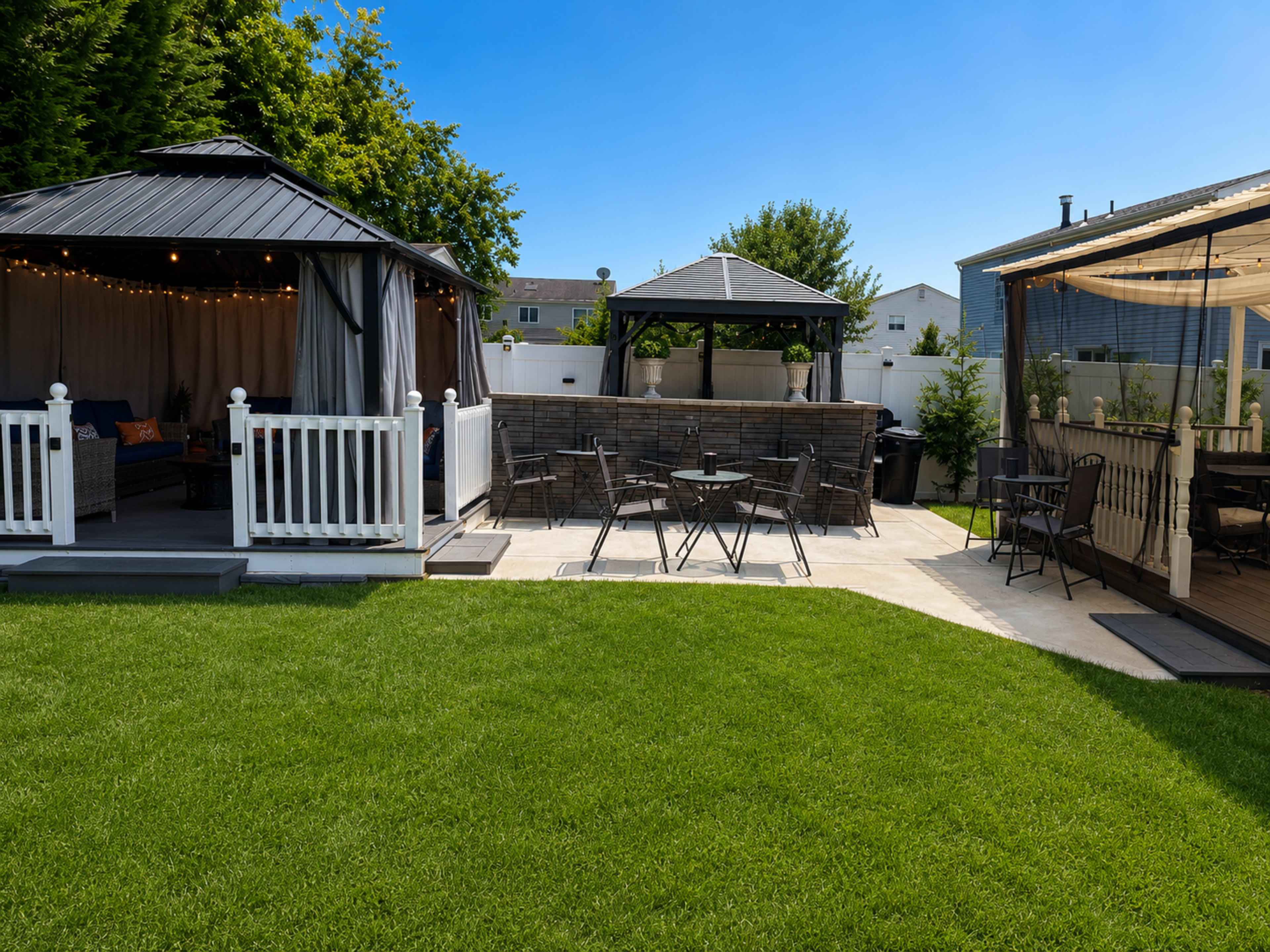 The image shows a well-manicured backyard featuring two gazebos, seating areas, and a neatly paved patio surrounded by green grass.