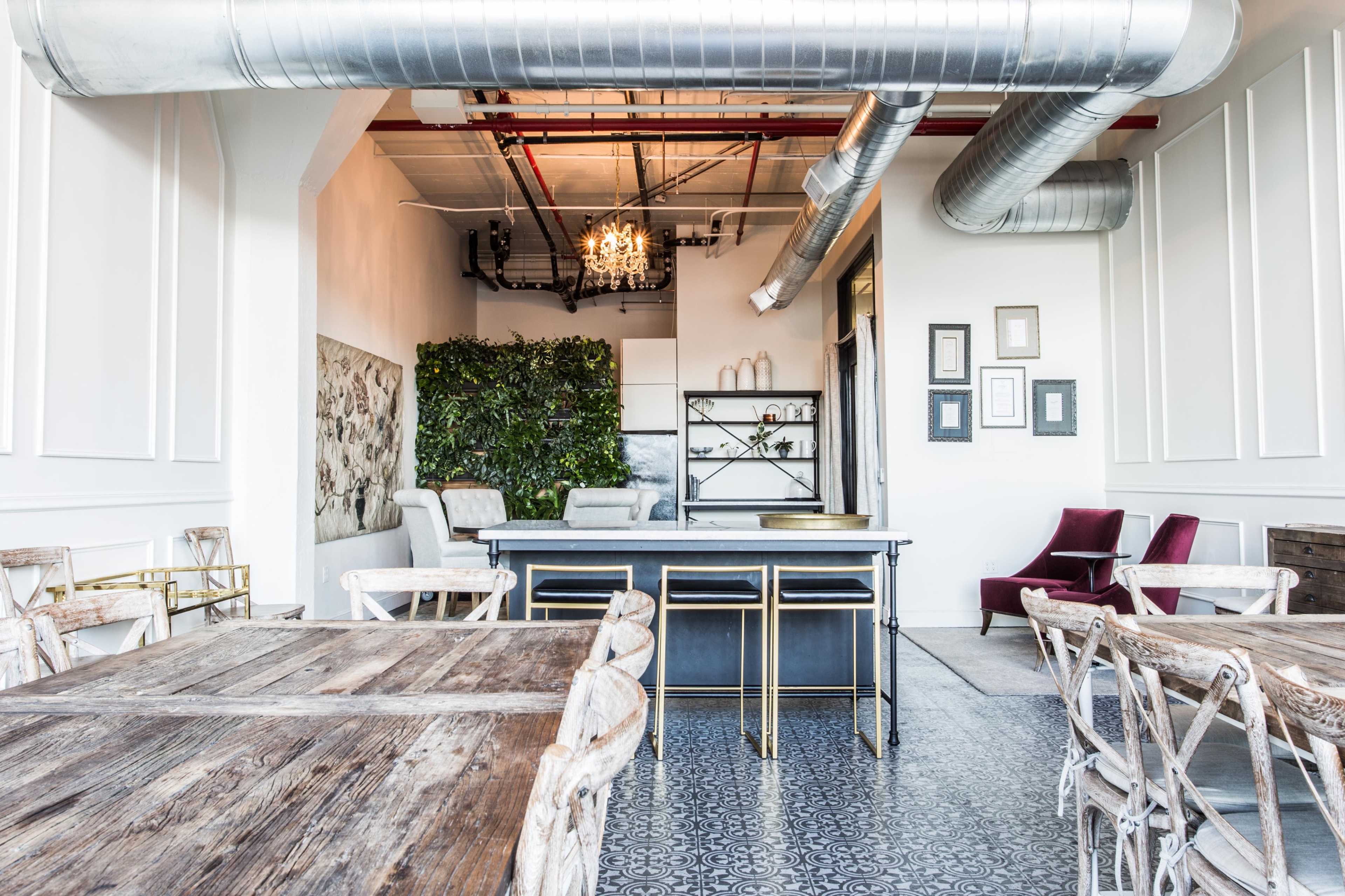 A stylish café interior with wooden tables, a sleek bar area, and green wall plants, complemented by decorative artwork on the walls.
