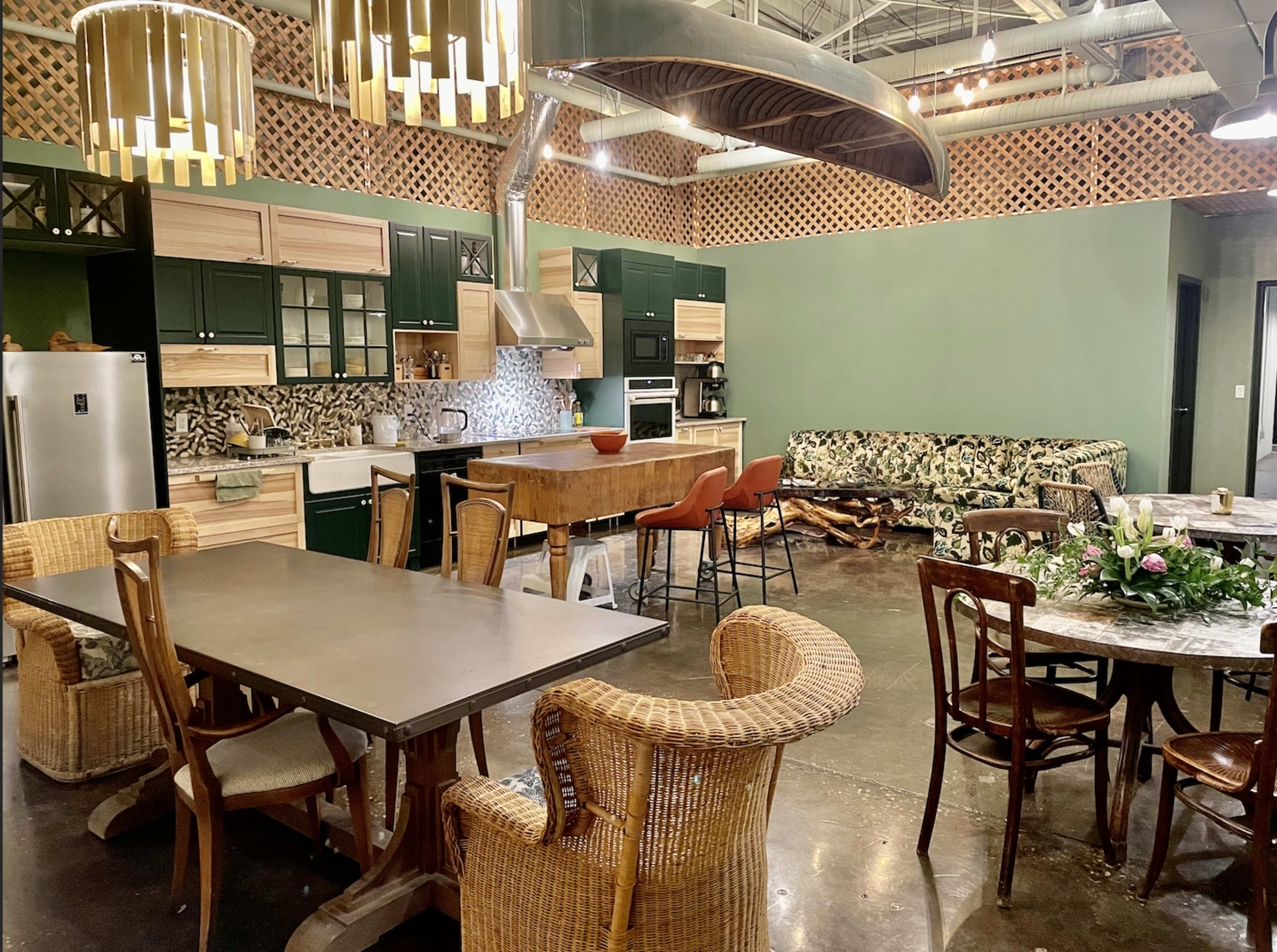 The image shows a spacious kitchen and dining area featuring modern furniture, a large table, and a colorful patterned sofa against a green wall.
