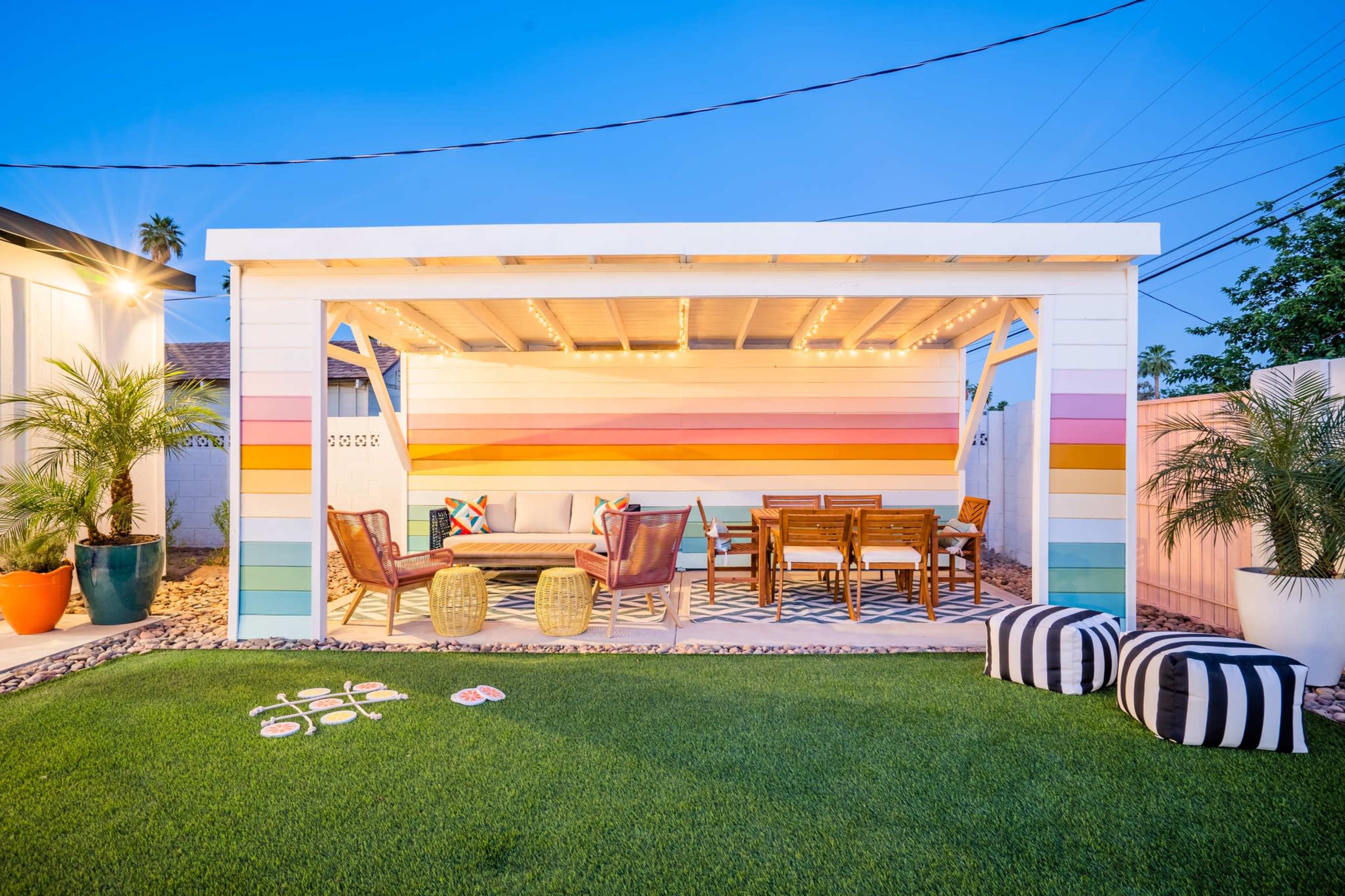 A brightly colored outdoor pavilion with comfortable seating, a dining area, and decorative elements surrounded by lush green grass and plants.