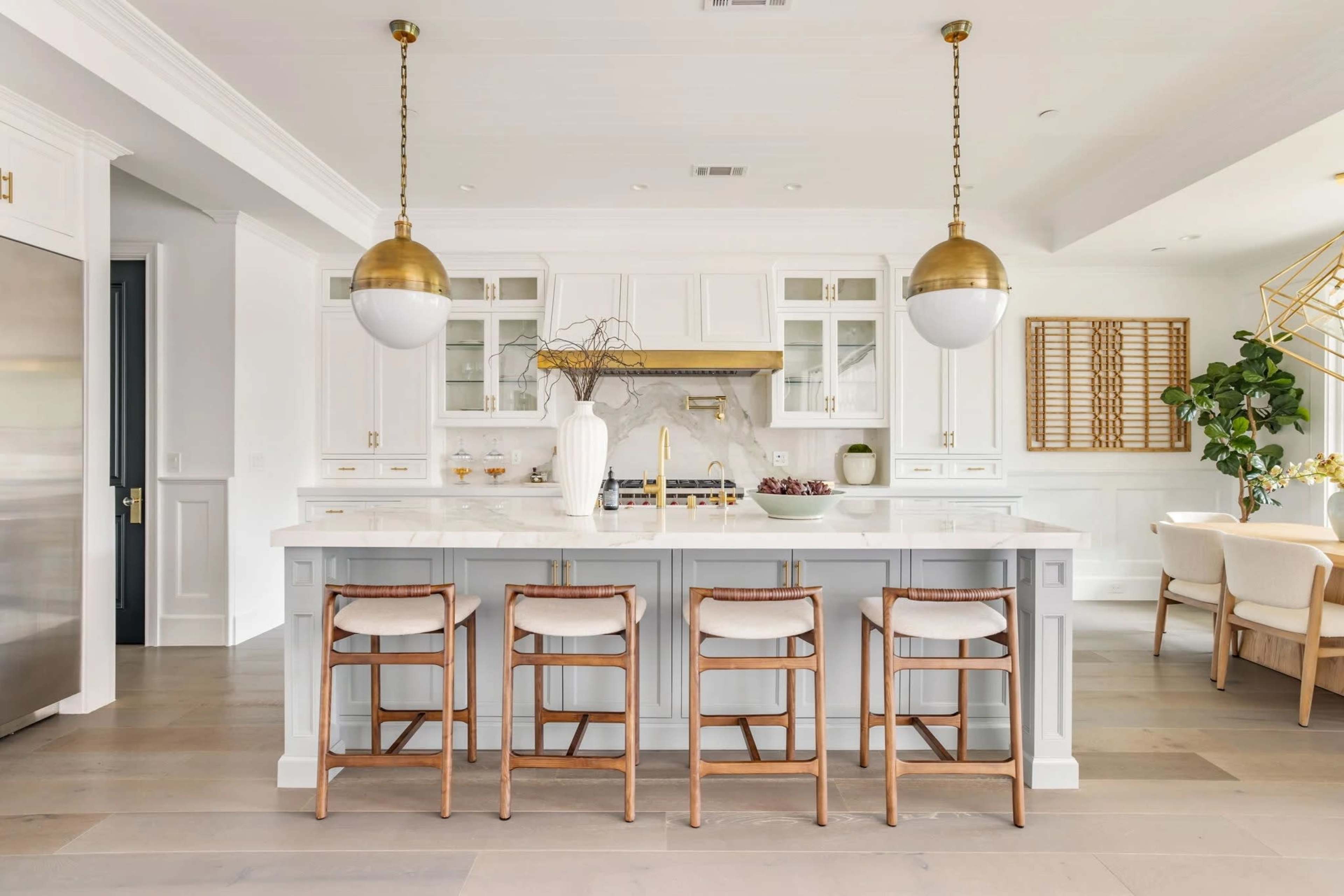A modern kitchen features white cabinetry, a large marble island with seating, and pendant lighting.