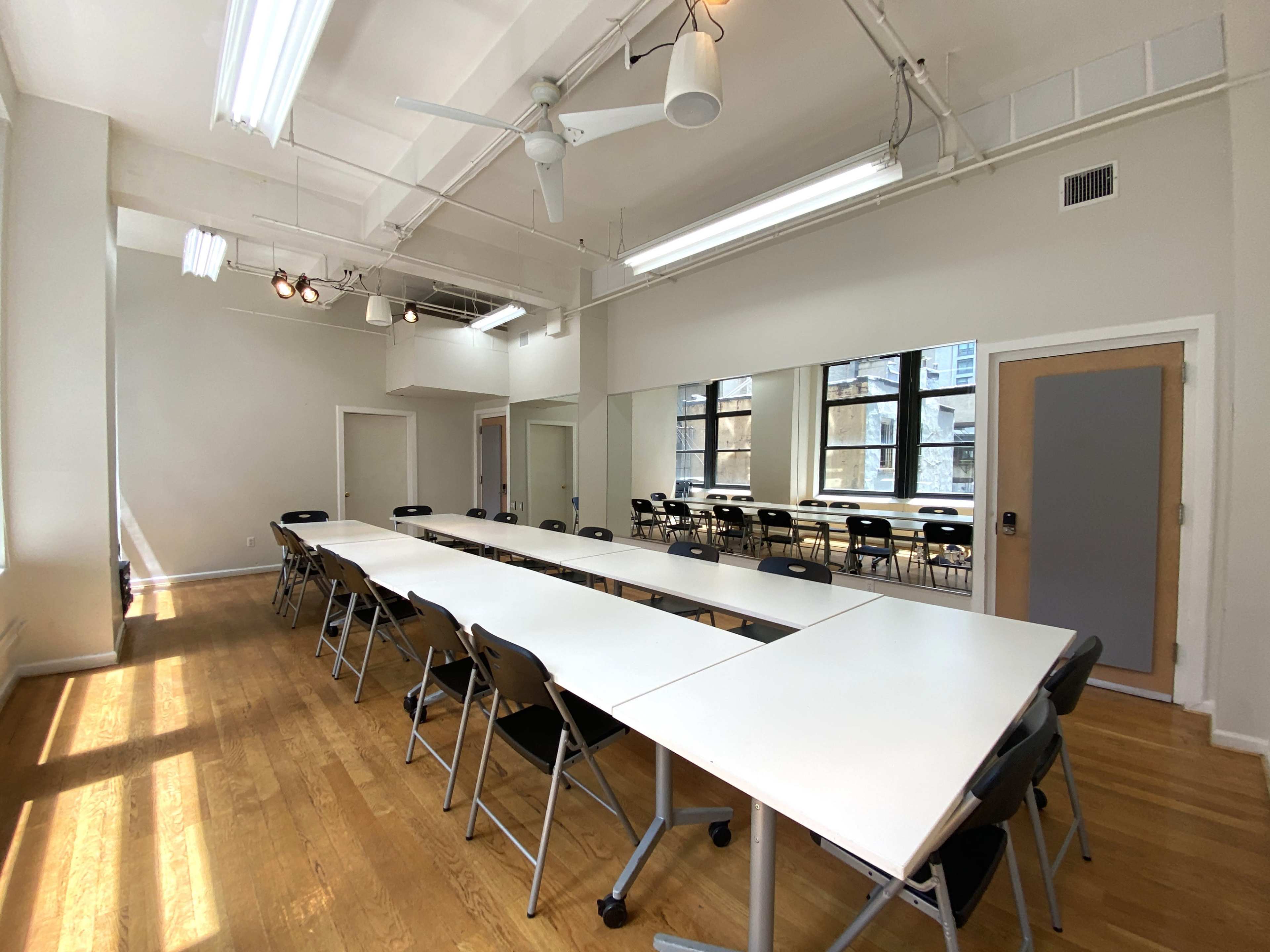 A spacious meeting room features a long table surrounded by black chairs, with large windows providing natural light.