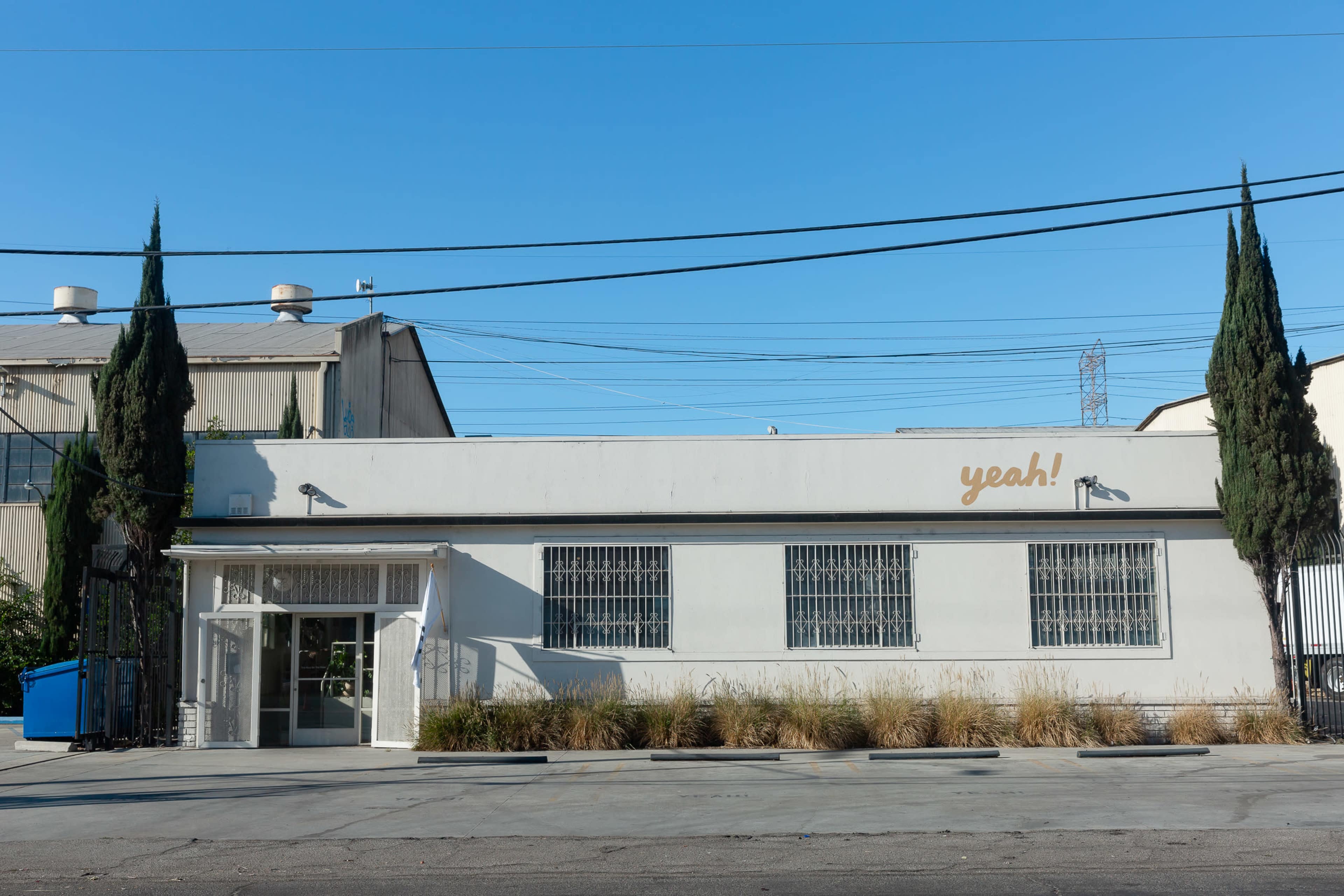 A single-story white building with barred windows features the word "yeah!" painted in gold on its exterior.