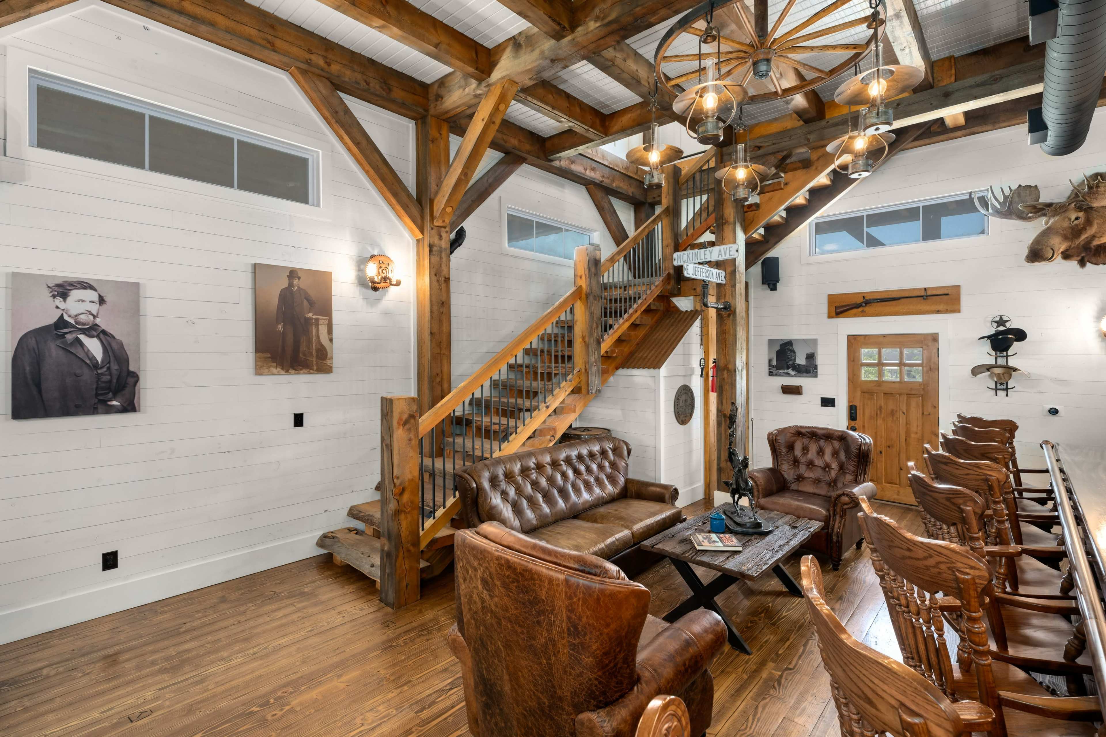 The interior features a rustic lounge area with leather seating, wooden beams, and a staircase, complemented by vintage photographs and a bar counter.