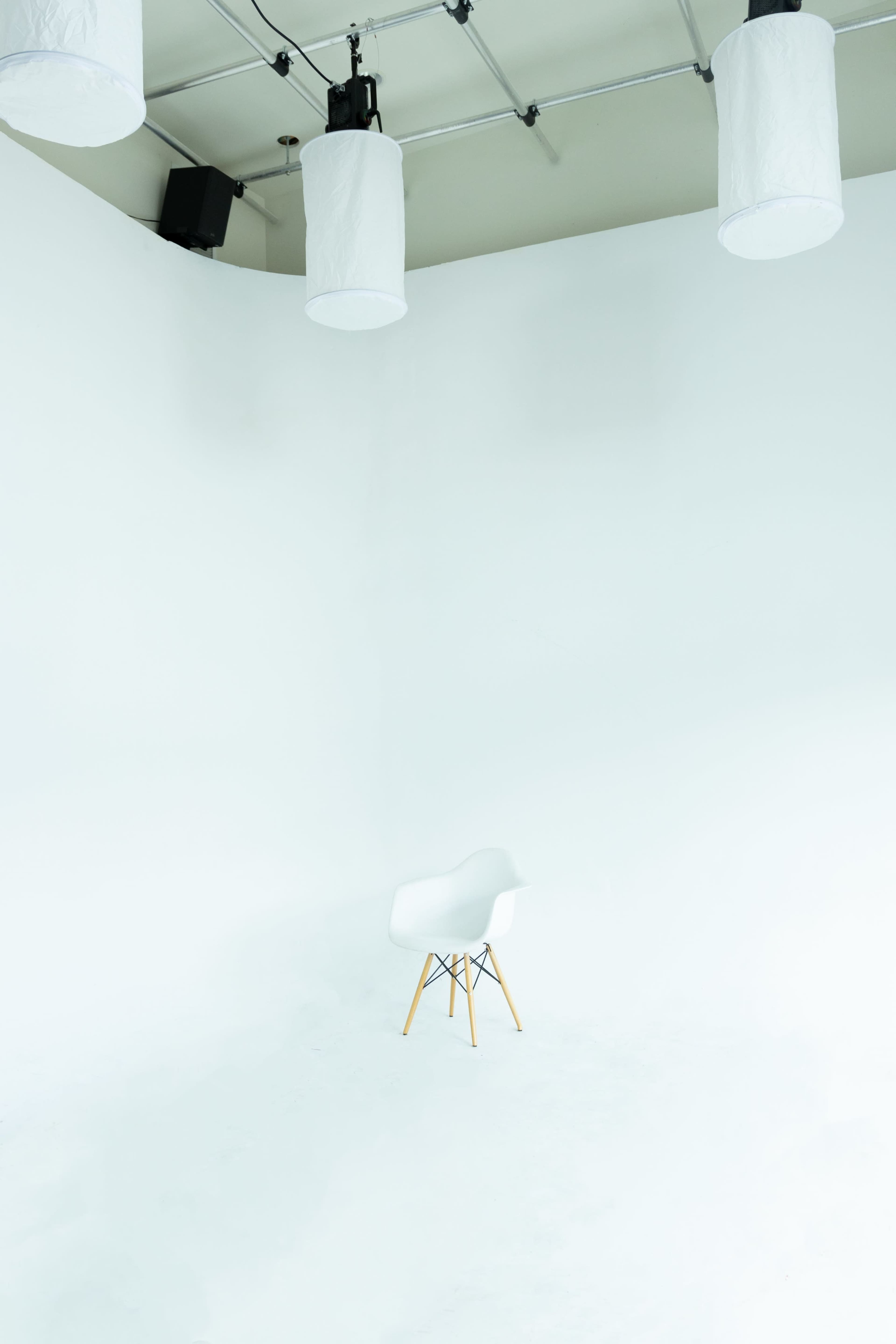 A white Eames chair is positioned in the center of a brightly lit, empty studio space with white walls.