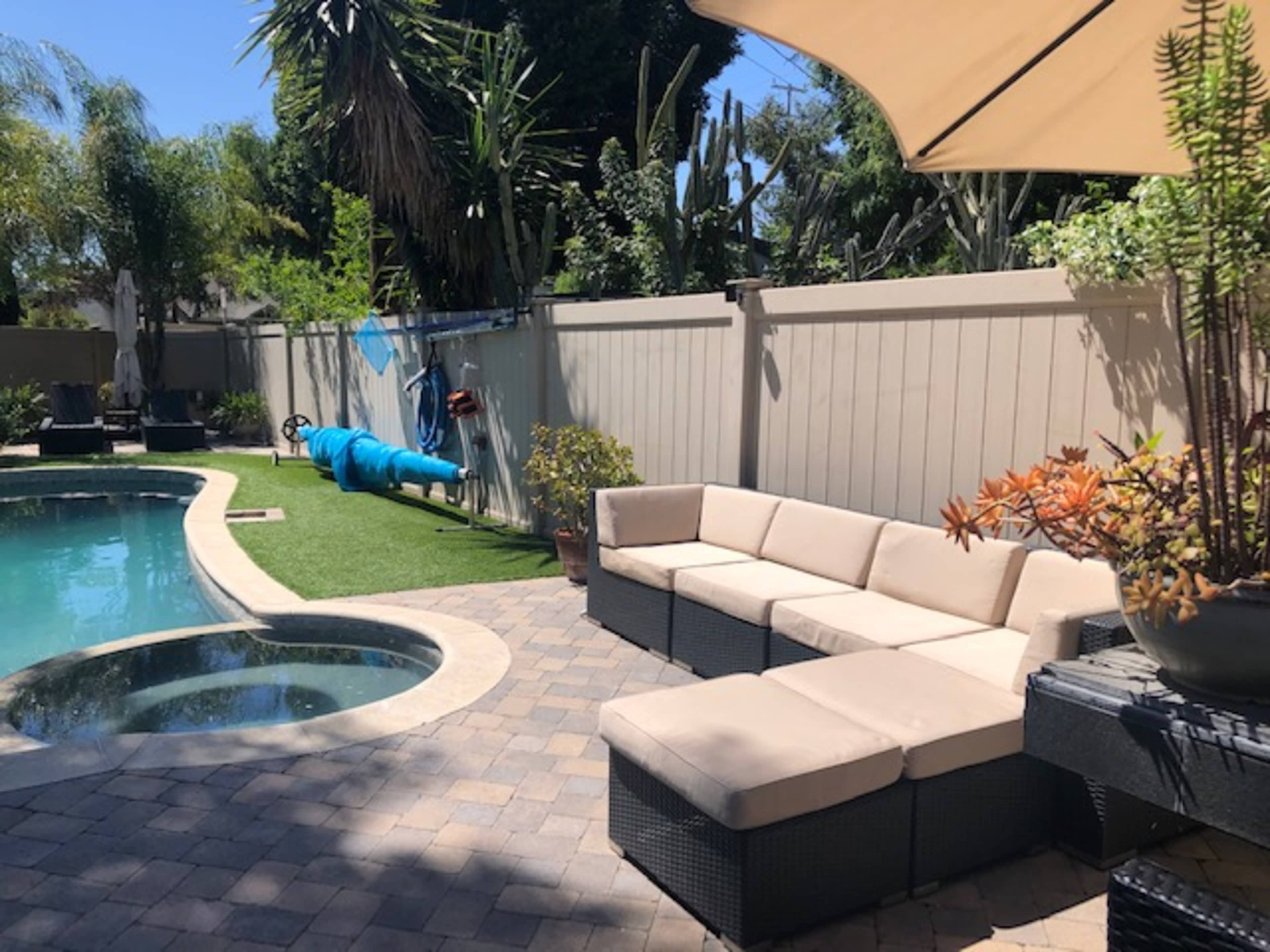 A backyard features a pool, a seating area with beige cushions, and a clothesline with blue items hanging in a sunny setting.
