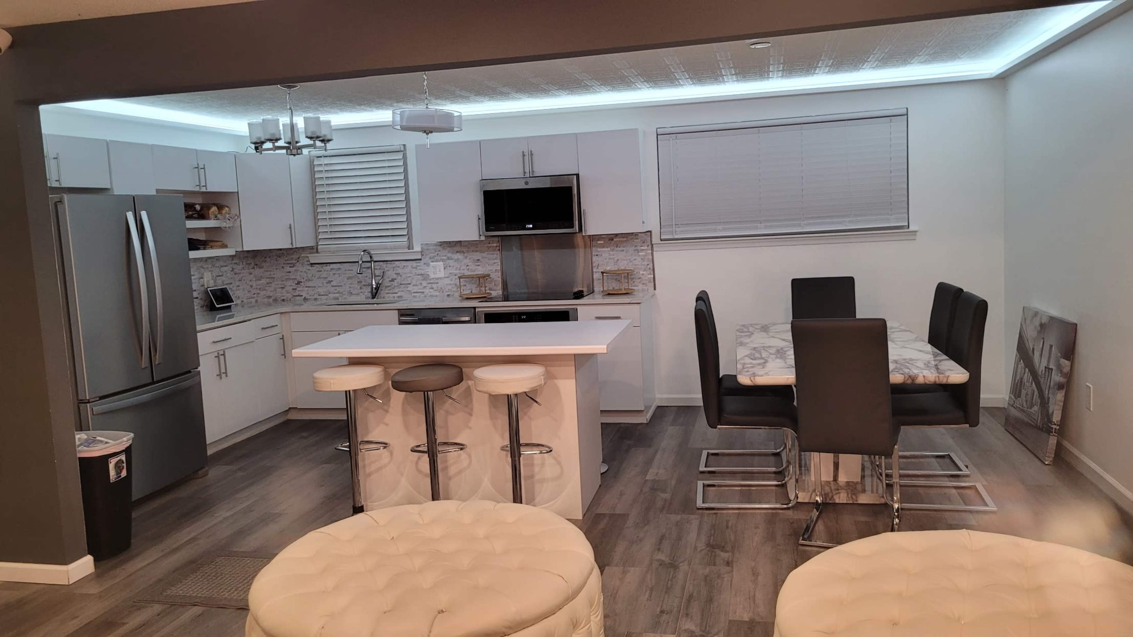 A modern kitchen with white cabinetry, stainless steel appliances, a breakfast bar with stools, and a dining table with black chairs.