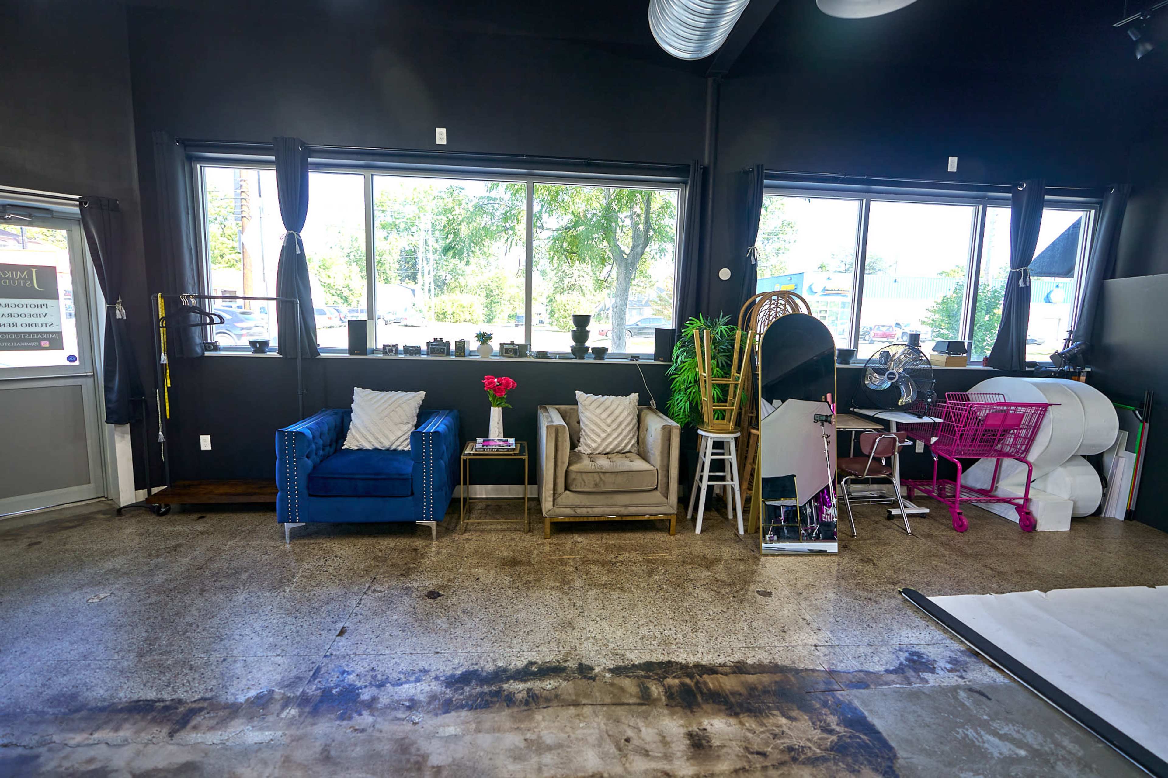 A modern interior space features two armchairs, a coffee table, and various decorative items near large windows, with a polished concrete floor.
