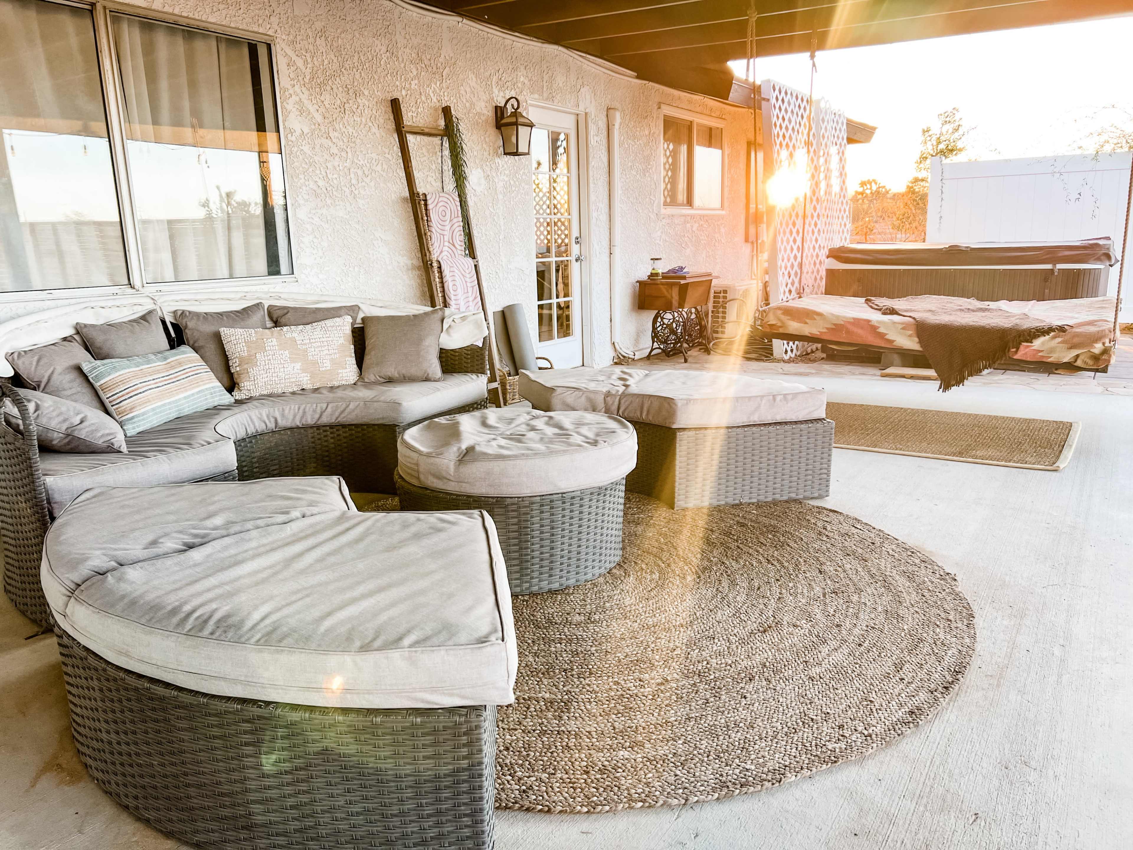 A patio area with a sectional sofa, round ottomans, and a cozy rug, illuminated by soft sunlight.
