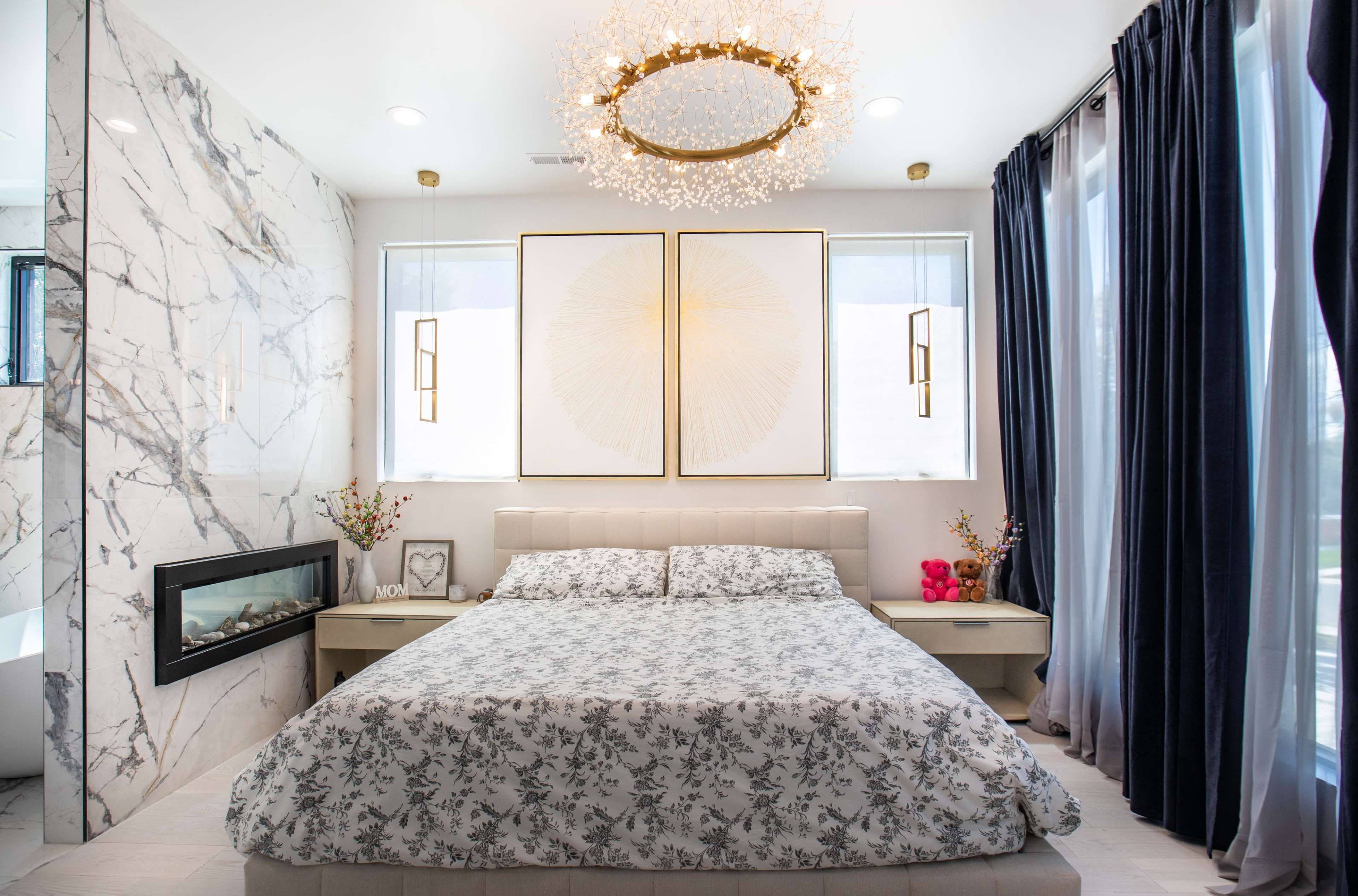 A contemporary bedroom with a bed featuring a floral-patterned bedspread, decorative artwork on the walls, and a modern chandelier above.