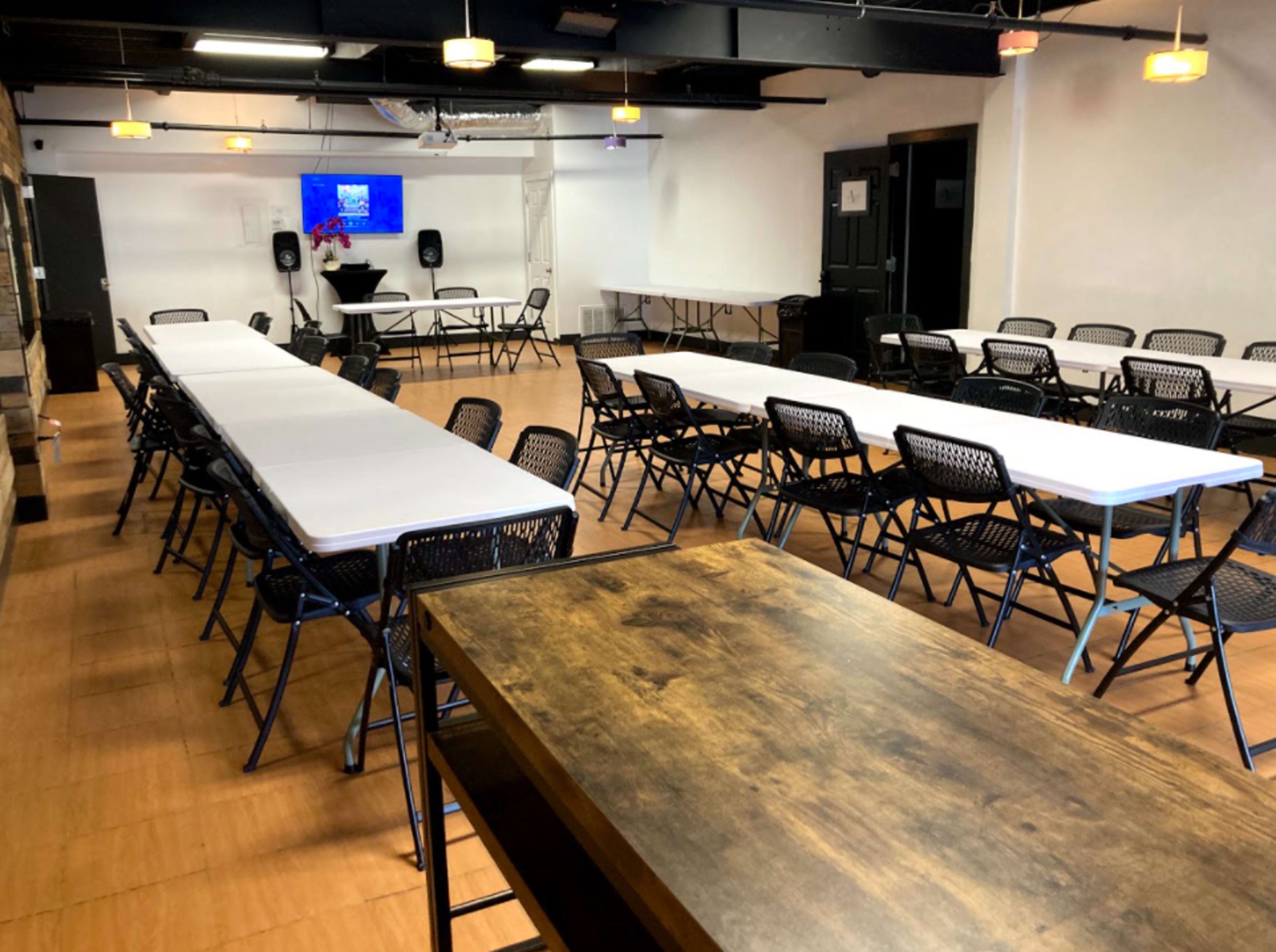 A spacious conference room features rows of folding tables and chairs arranged for an event, with a presentation screen at the front.