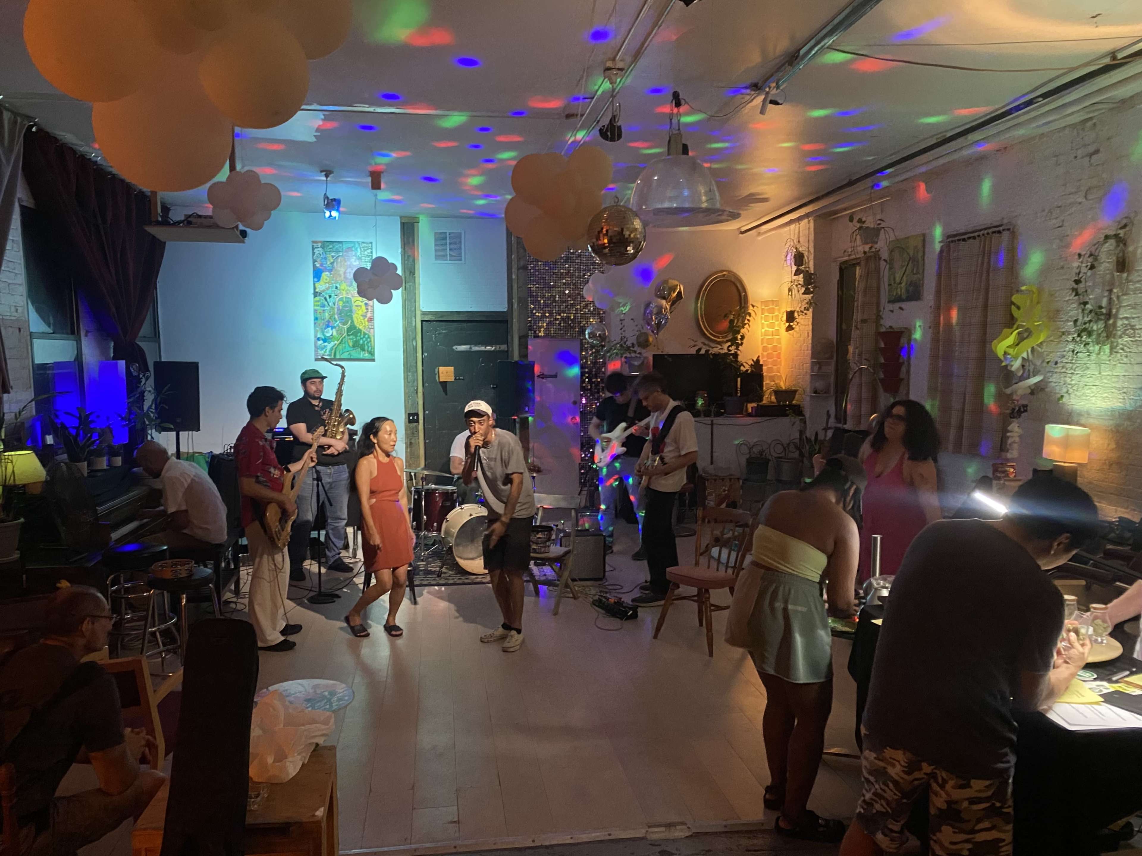 A diverse group of people performs music and socializes in a decorated indoor space with colorful lights and decorations for a lively gathering.