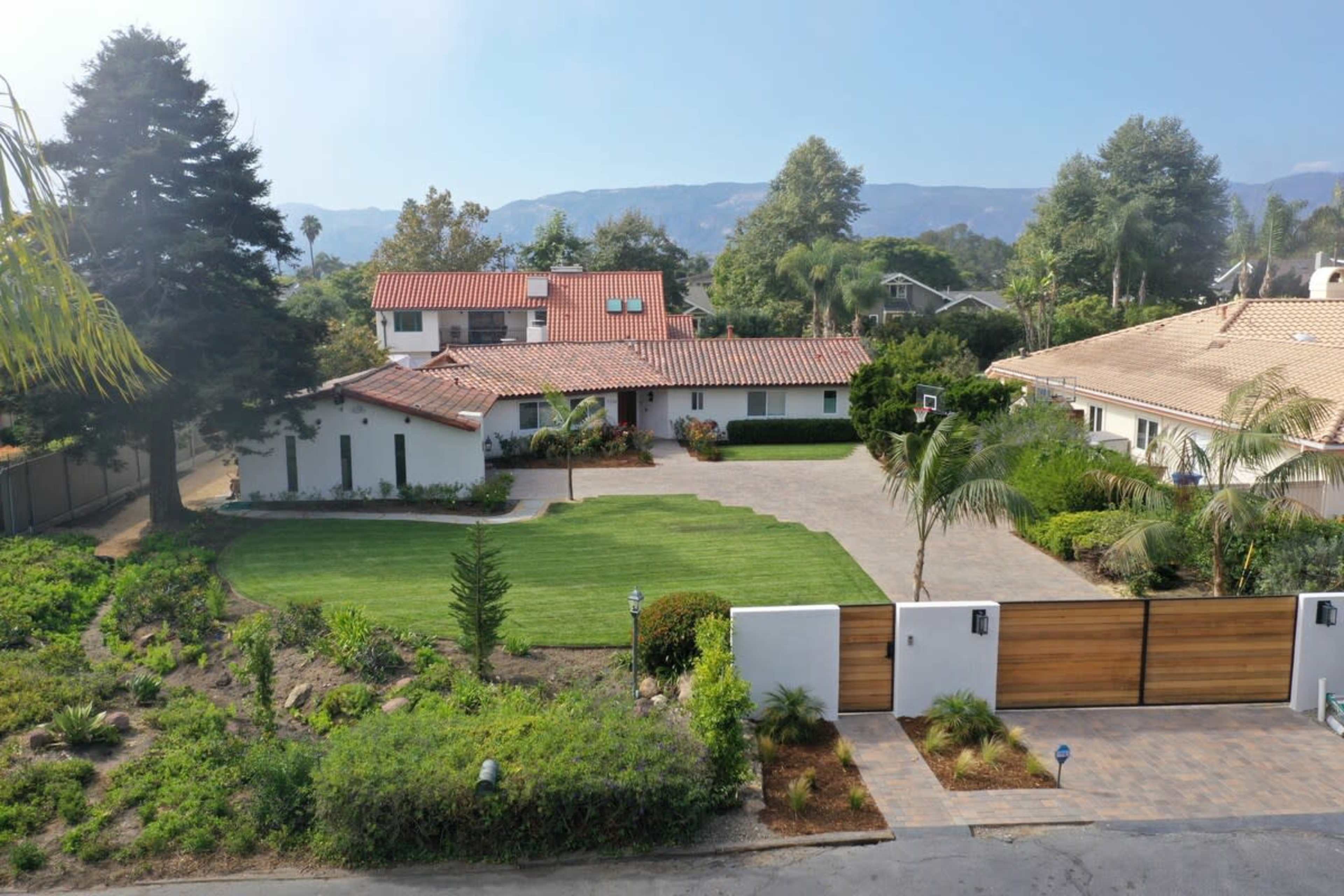 A spacious residential property featuring a landscaped yard, a paved driveway, and nearby mountains in the background.