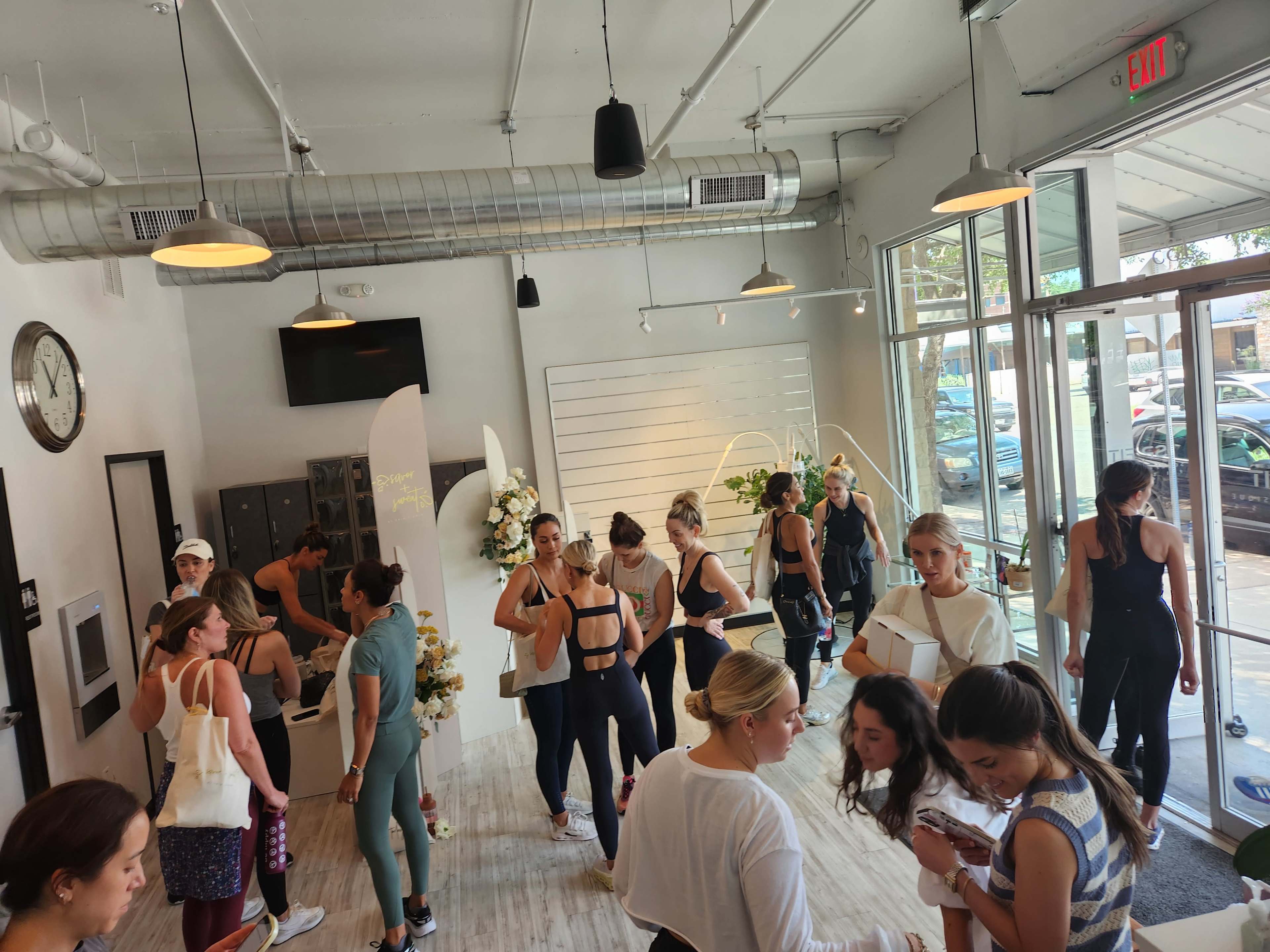 A busy fitness studio interior shows multiple individuals engaging in various activities, with some socializing and others preparing for a workout.