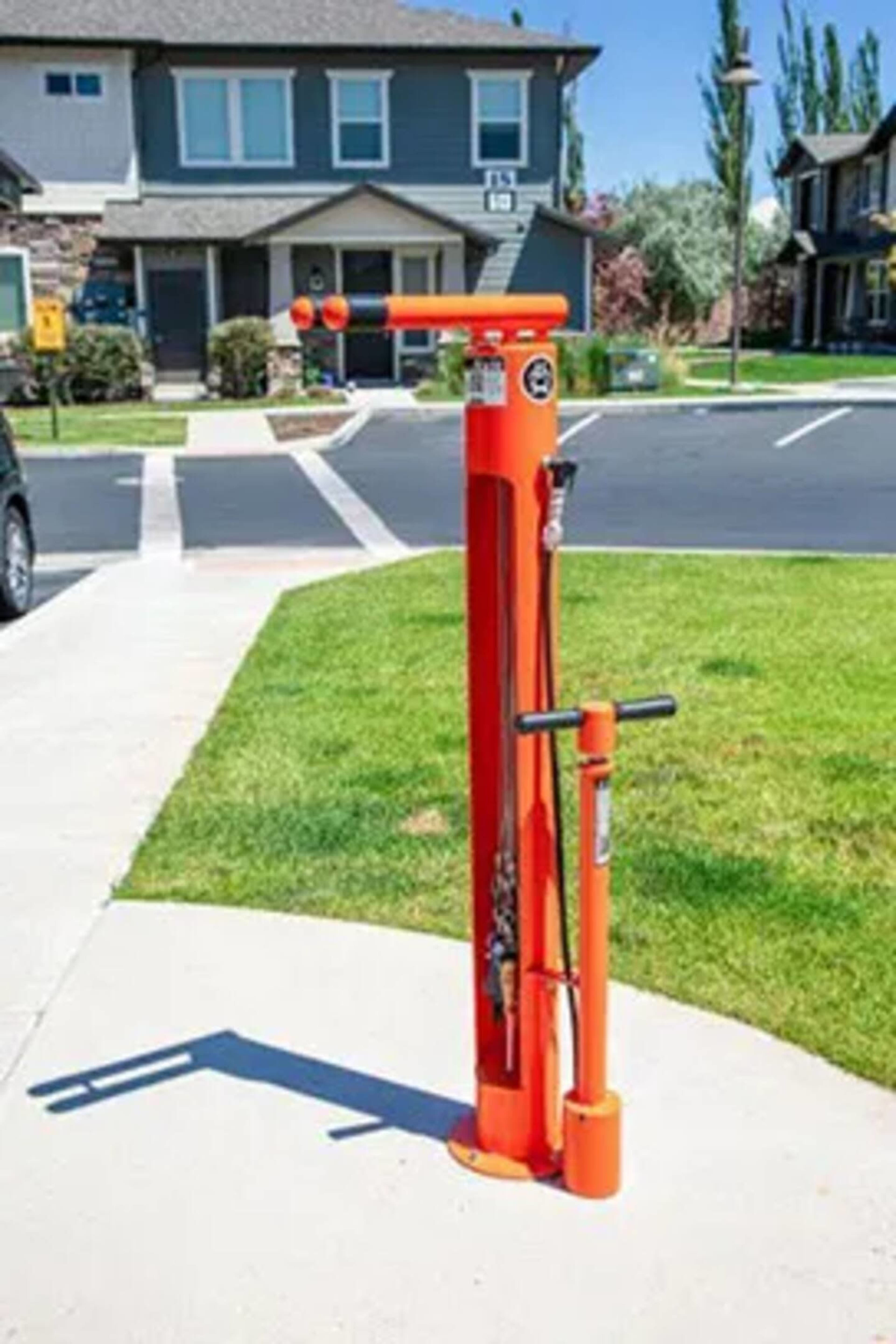 An orange bicycle repair station with tools mounted on a post, located on a paved path near residential buildings.
