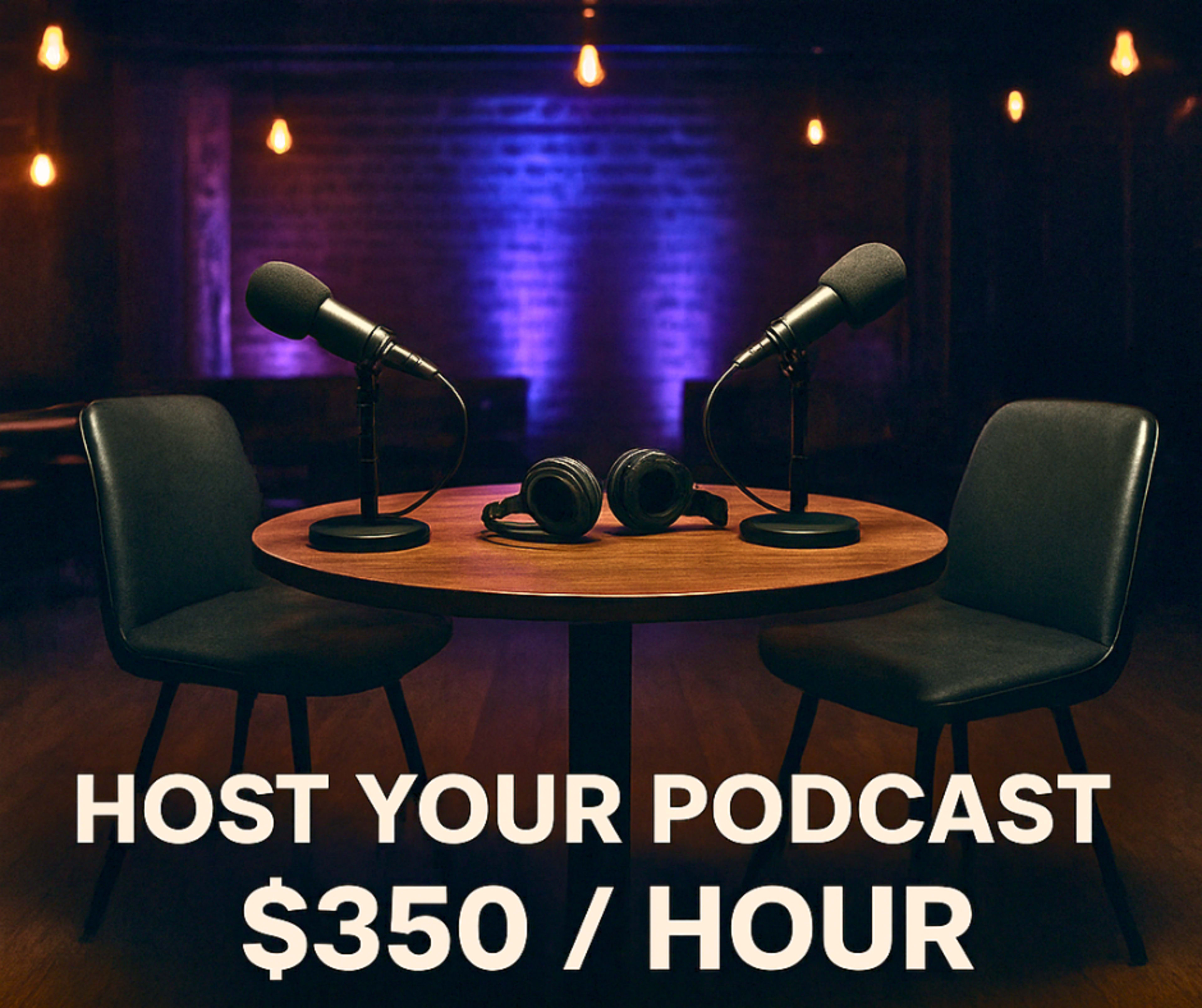 A table with two microphones and headphones sits between two empty chairs in a dimly lit recording studio.