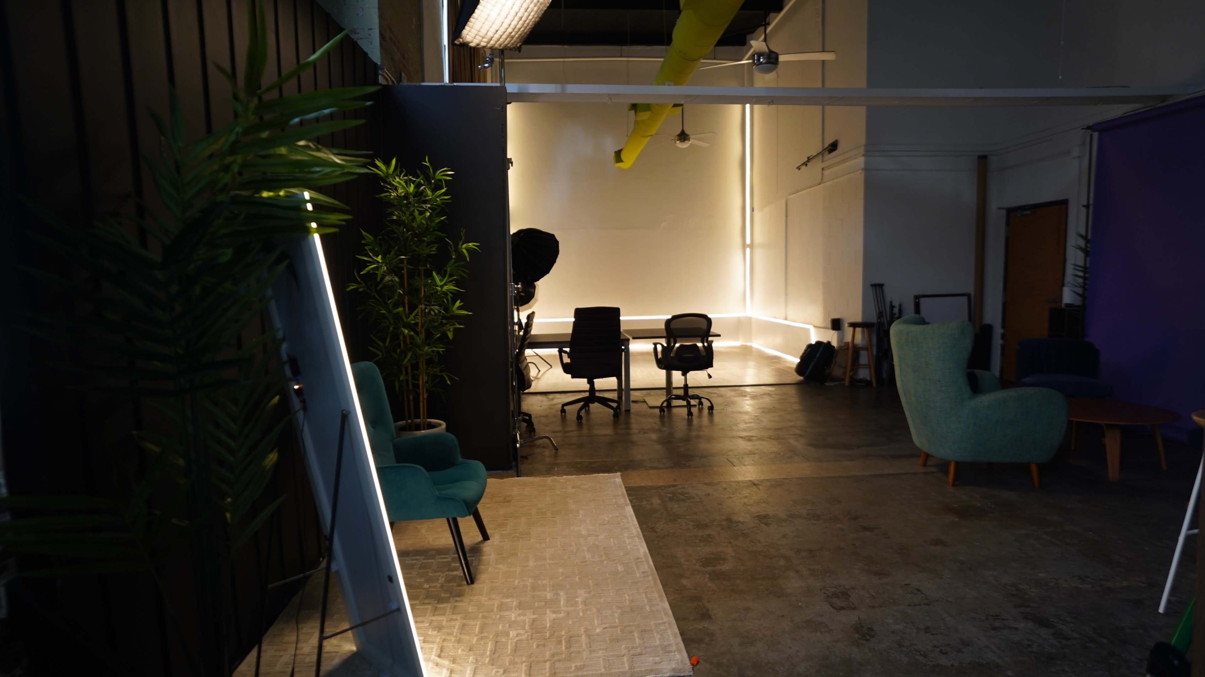 The image shows a modern, open studio space with a mirrored wall, chairs, and a table, illuminated by soft, ambient lighting.